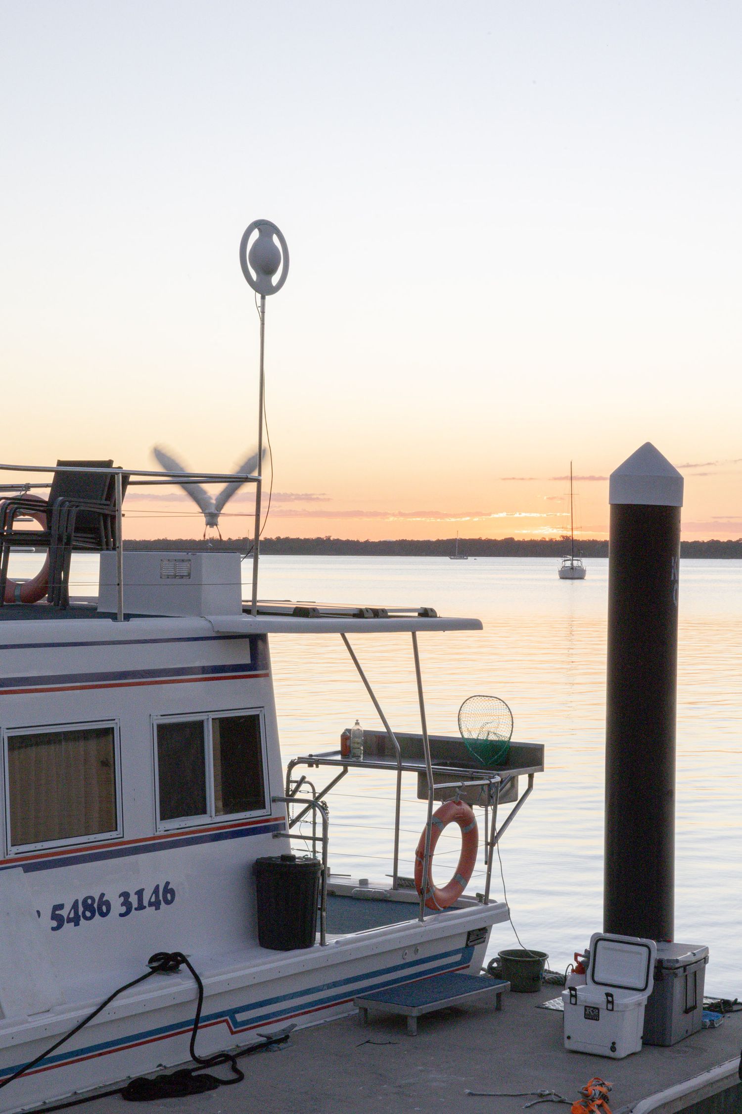 Fishing boat docked at marina during sunset with navigation markers visible.