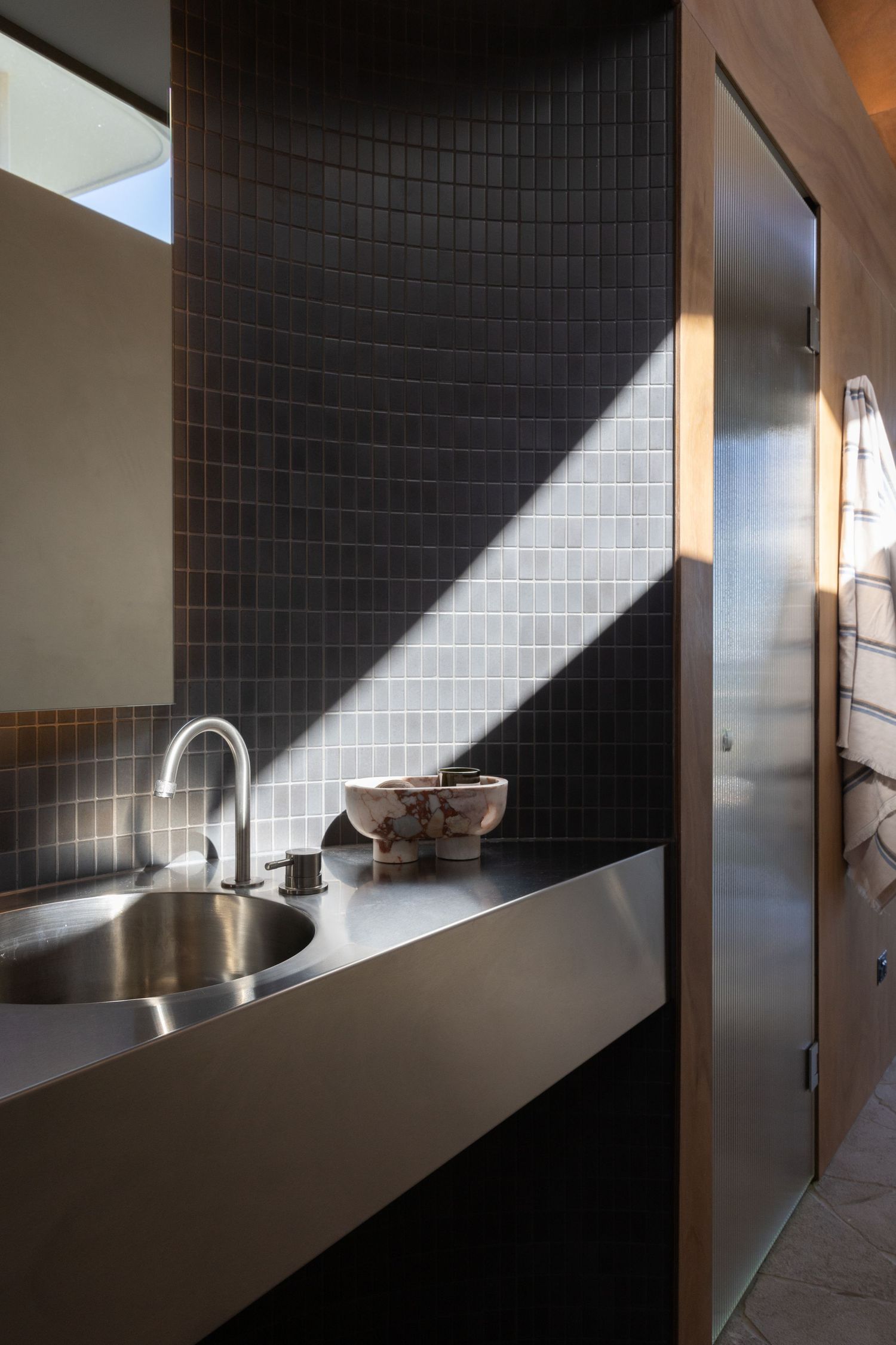 Dramatic angular shadows dance across dark tiled walls in a modern interior hallway with natural light streaming in.