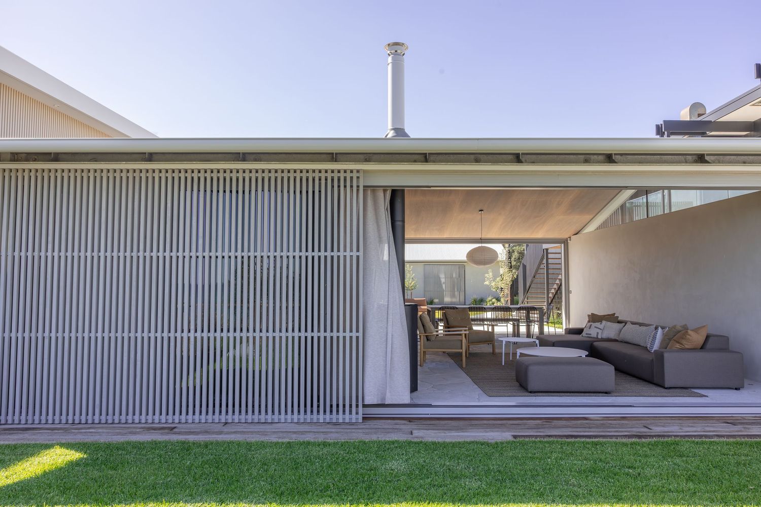 Modern mid-century home exterior with large windows and sliding glass doors opens to a spacious outdoor patio area.