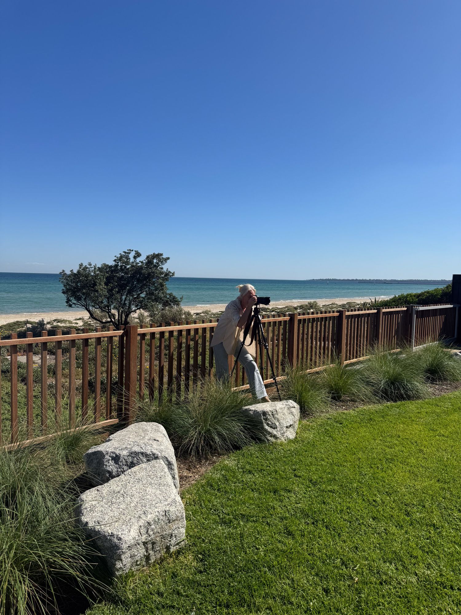 Coastal viewing area with wooden fence and large rocks overlooking blue ocean waters.