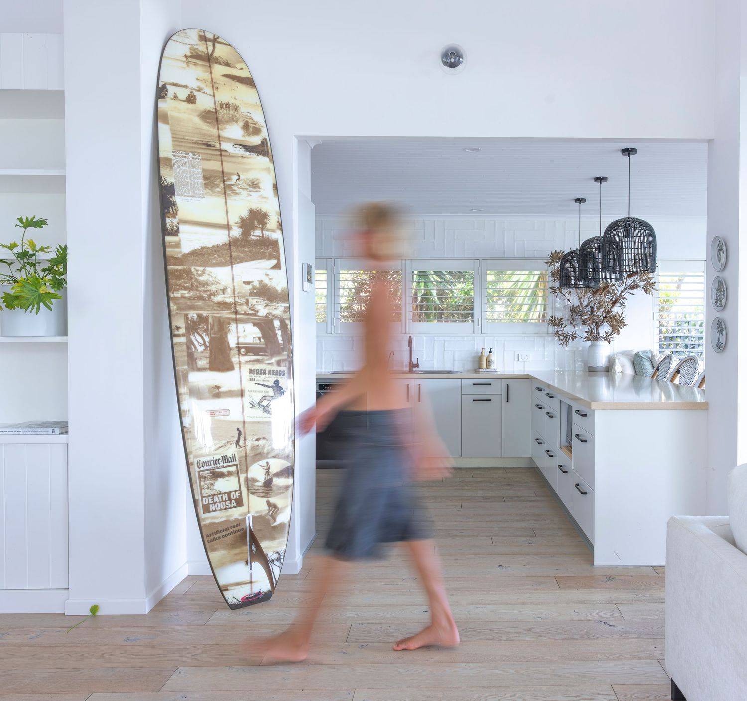 Time-lapse photo showing blurred motion of people walking through a modern white gallery space with wooden floors.