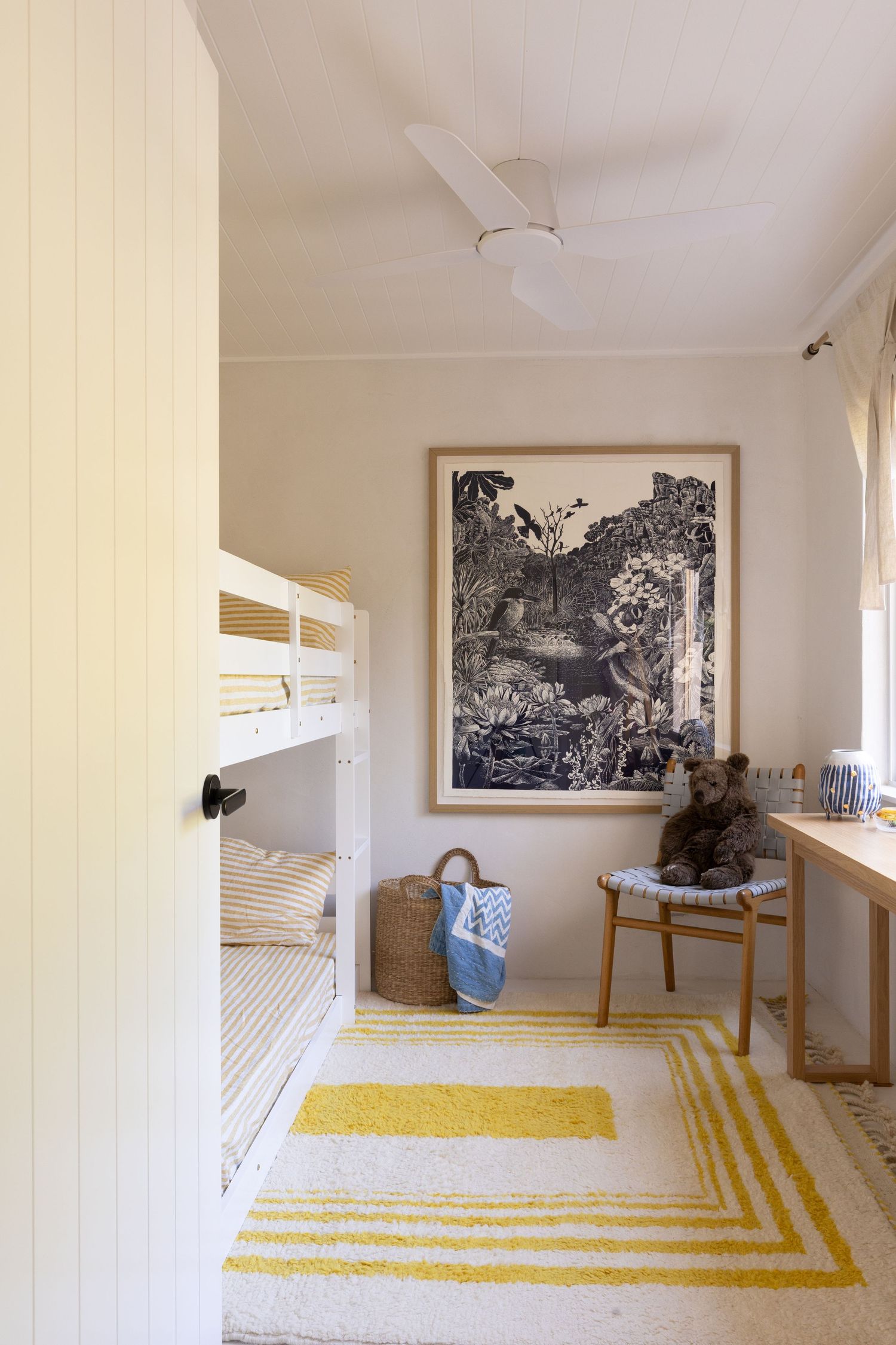 Modern kids bedroom with white bunk beds, yellow striped rug, and black and white framed artwork on cream walls.