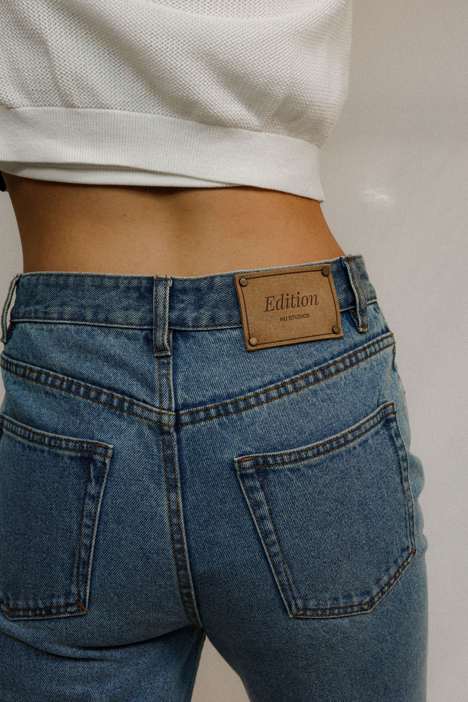 Close-up of blue denim jeans with brown leather Edition label patch on back waistband.