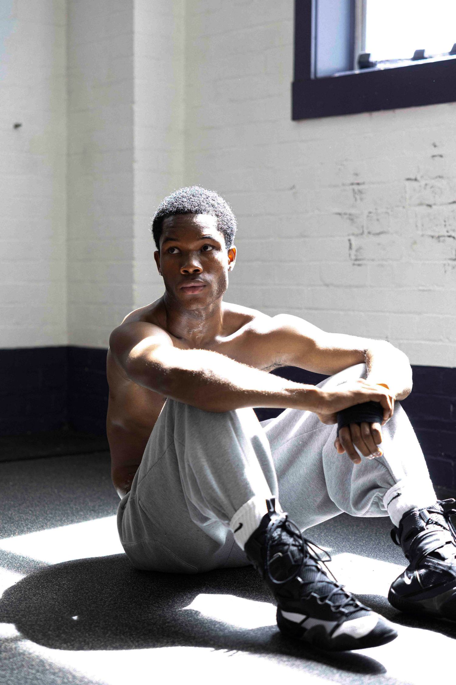 Athlete in casual wear sits on floor in sunlit gym corner.