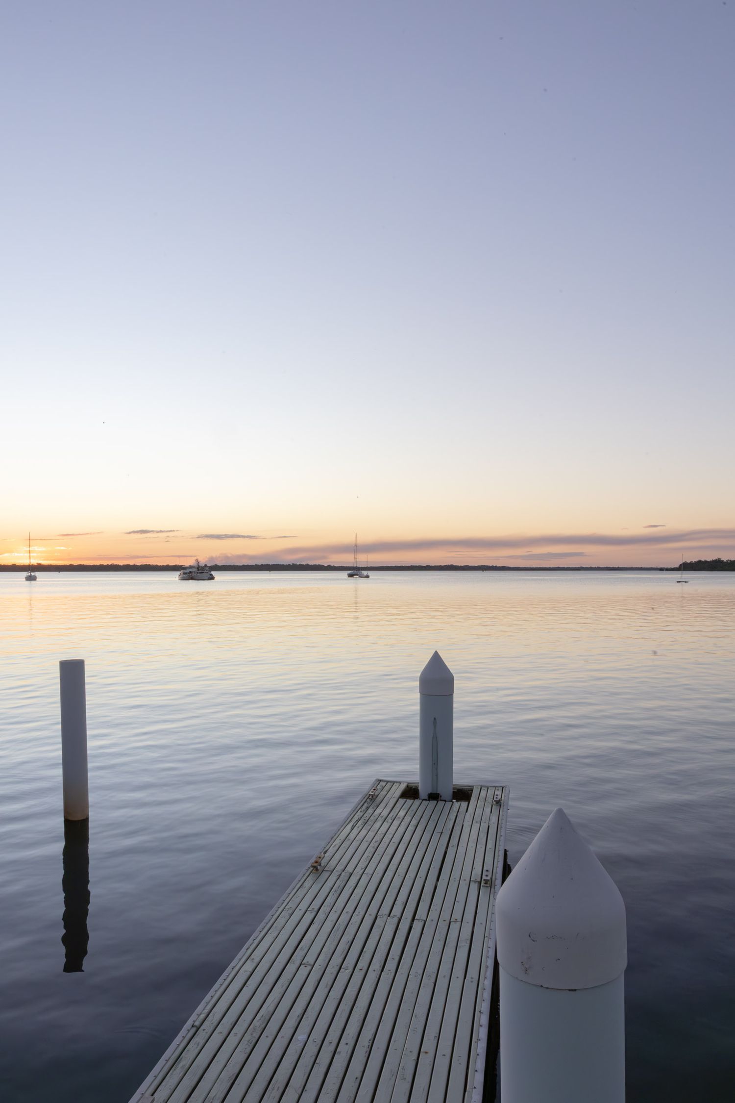 Serene marina view at dusk with wooden pier posts and boats anchored in distance.