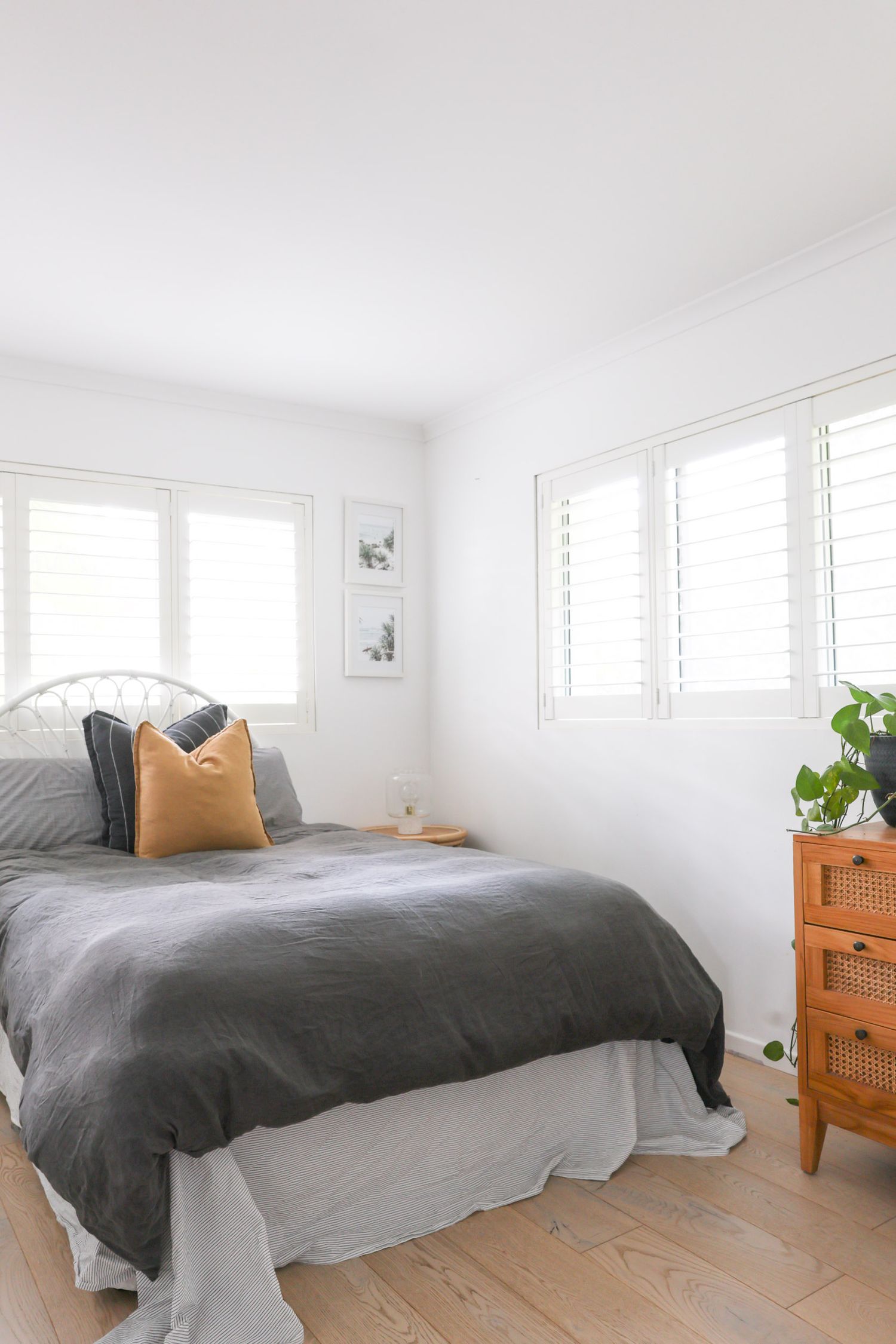 Serene bedroom featuring gray bedding, white shutters, and wooden storage unit.