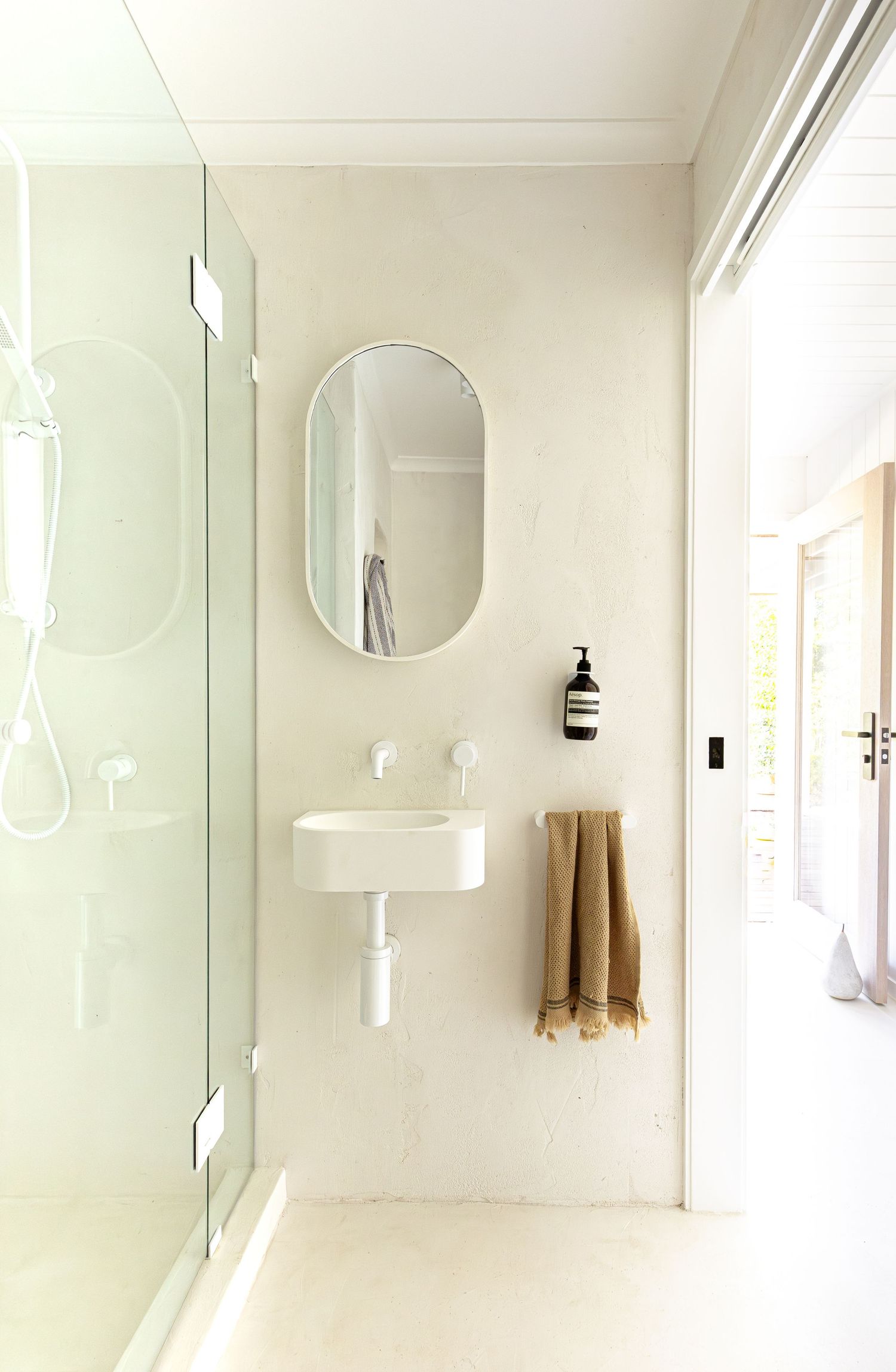 A bright white modern bathroom interior with round mirrors and natural light streaming through windows.