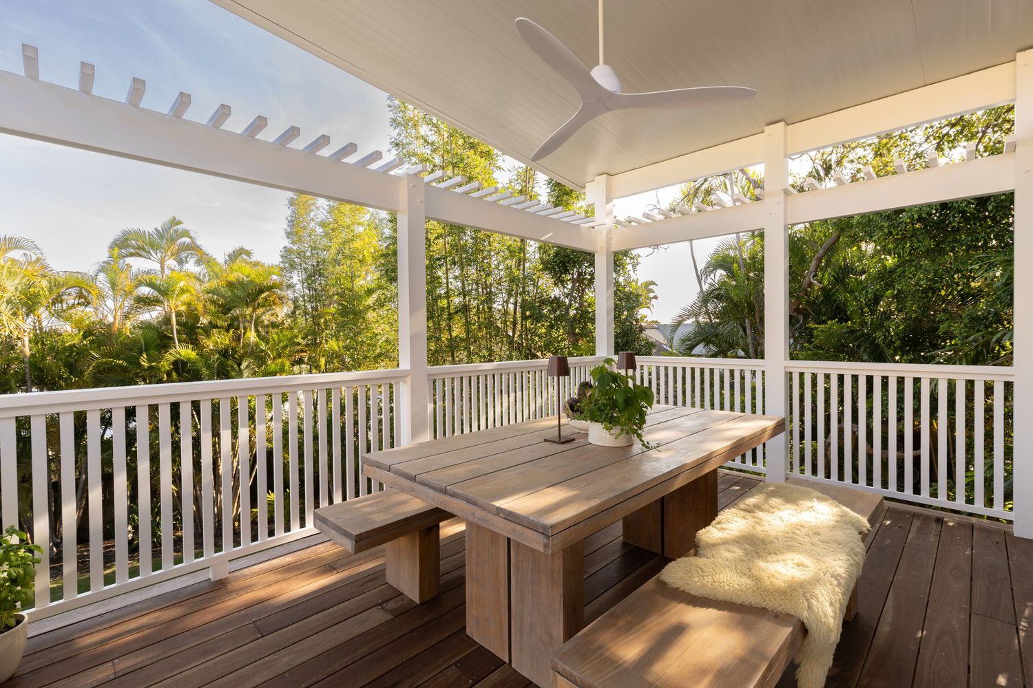 White wooden porch railing extends along a covered deck with sunlight filtering through trees in the background.