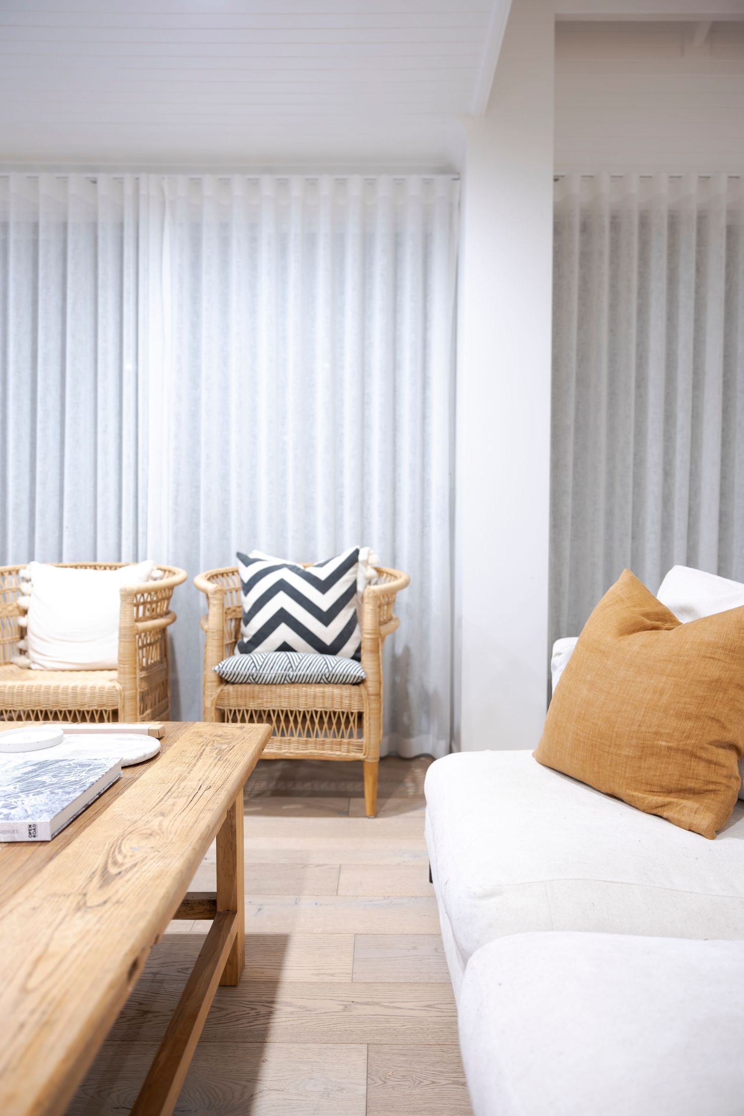 Modern wooden bench seating with white and chevron pattern cushions against vertical blinds in a minimalist space.