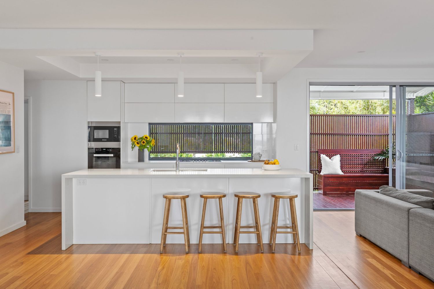 Modern white kitchen and dining area with gray sofa in an open concept living space features minimalist design elements.