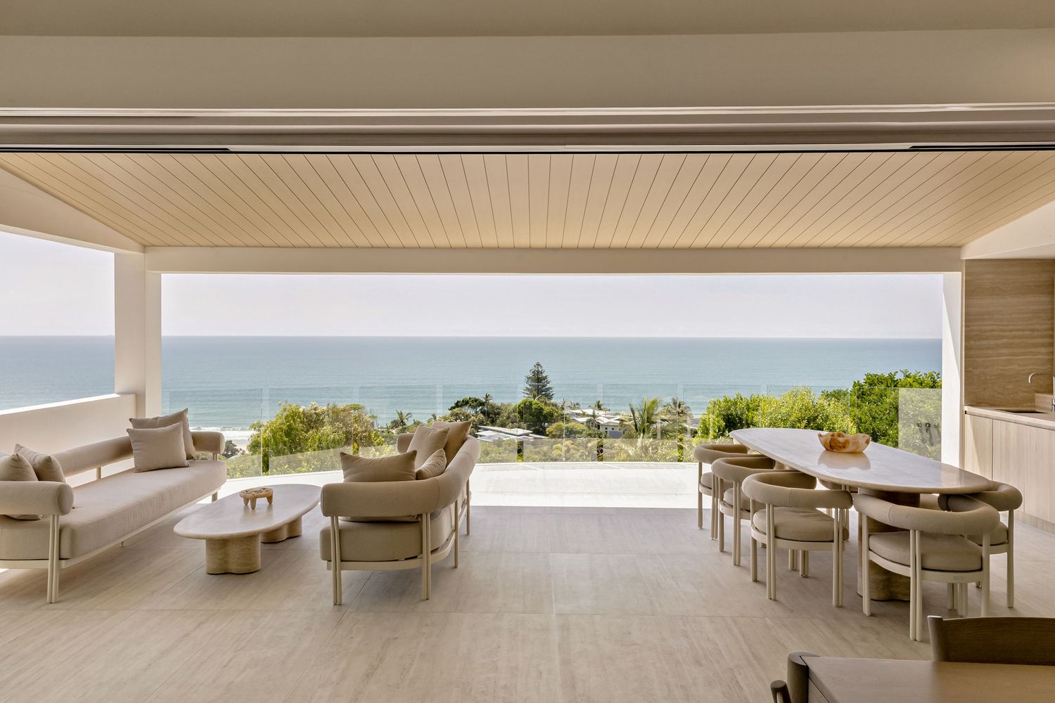 Luxury covered patio with ocean views, featuring neutral outdoor seating, dining area, and seamless indoor-outdoor living space.