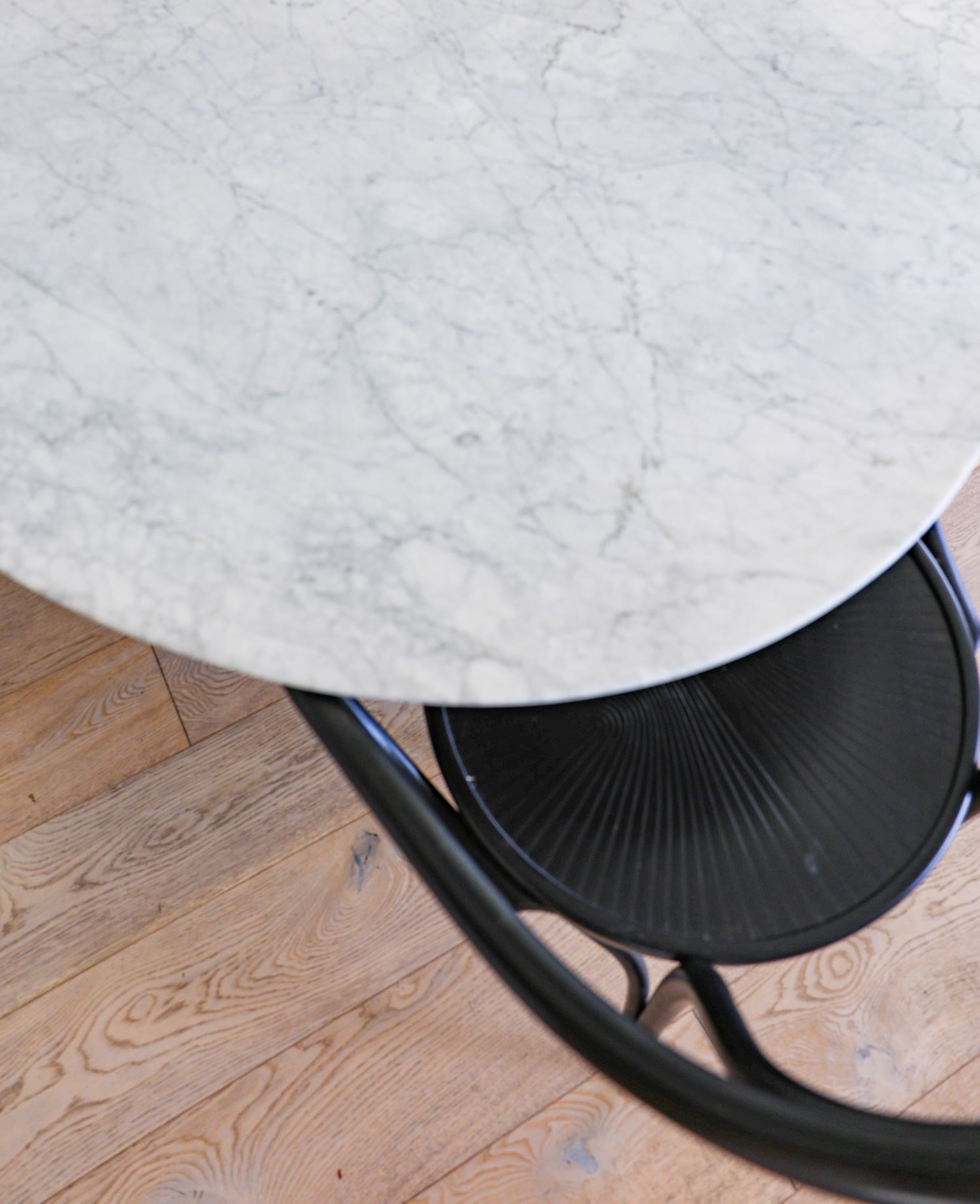 Marble table top detail with black modern base and wooden flooring.