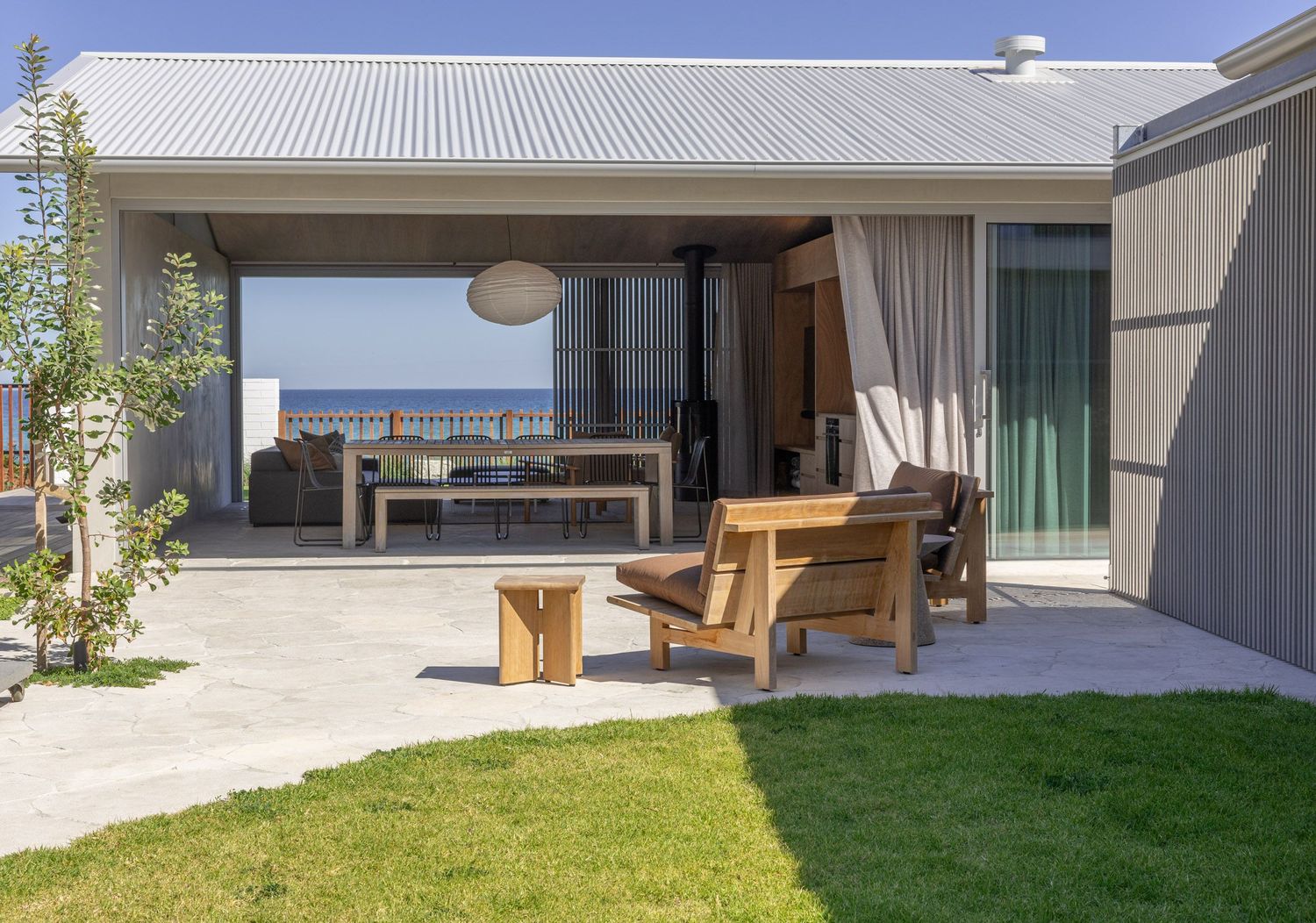 Modern beach house terrace featuring wooden outdoor furniture and seamless indoor-outdoor flow.
