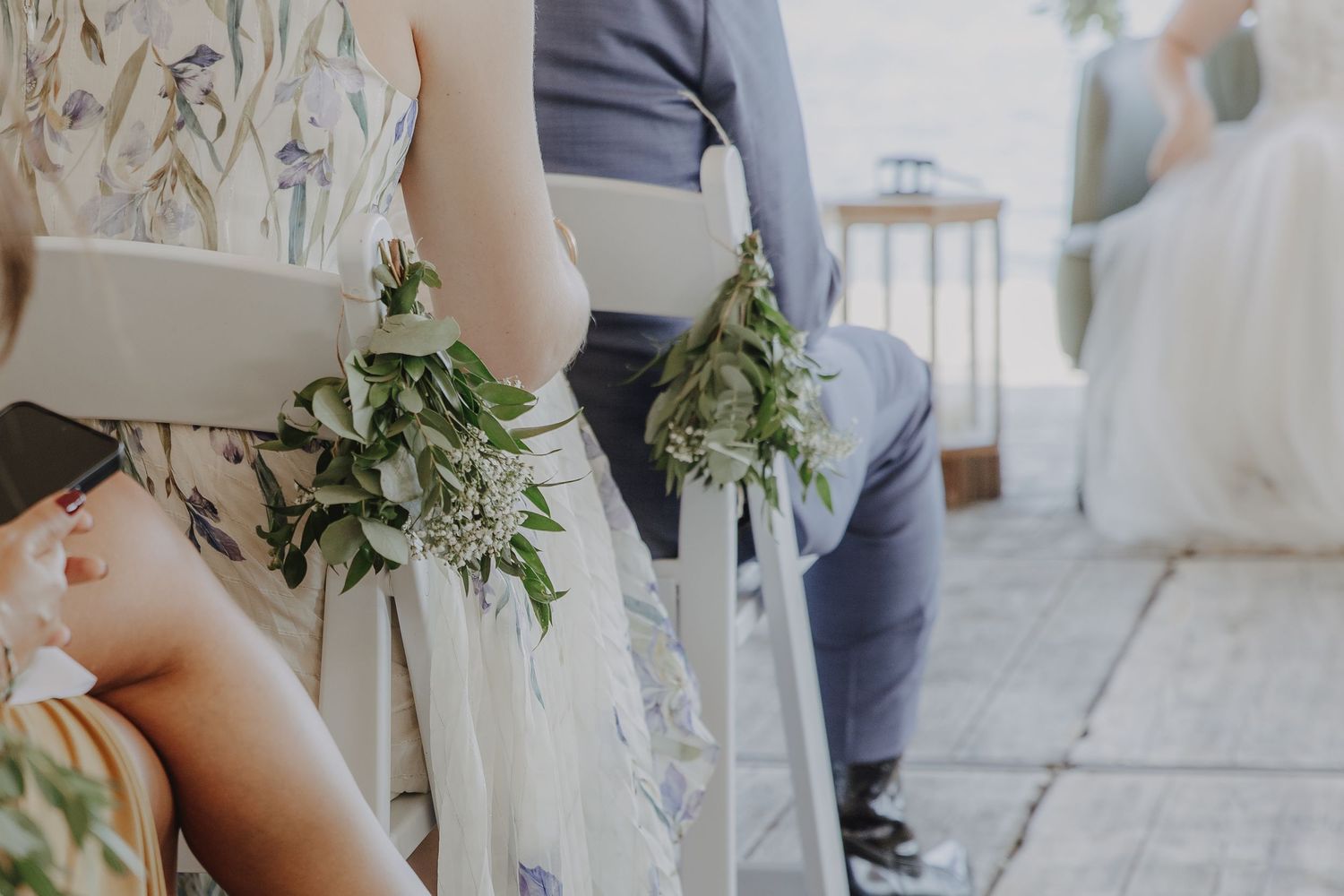 Wedding chairs adorned with elegant greenery bouquets tied with white ribbon at an outdoor ceremony.