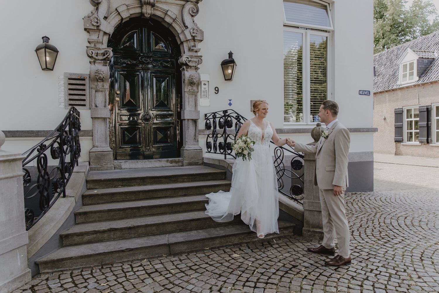 Bride and groom standing on cobblestone steps outside elegant venue with ornate door and lanterns.