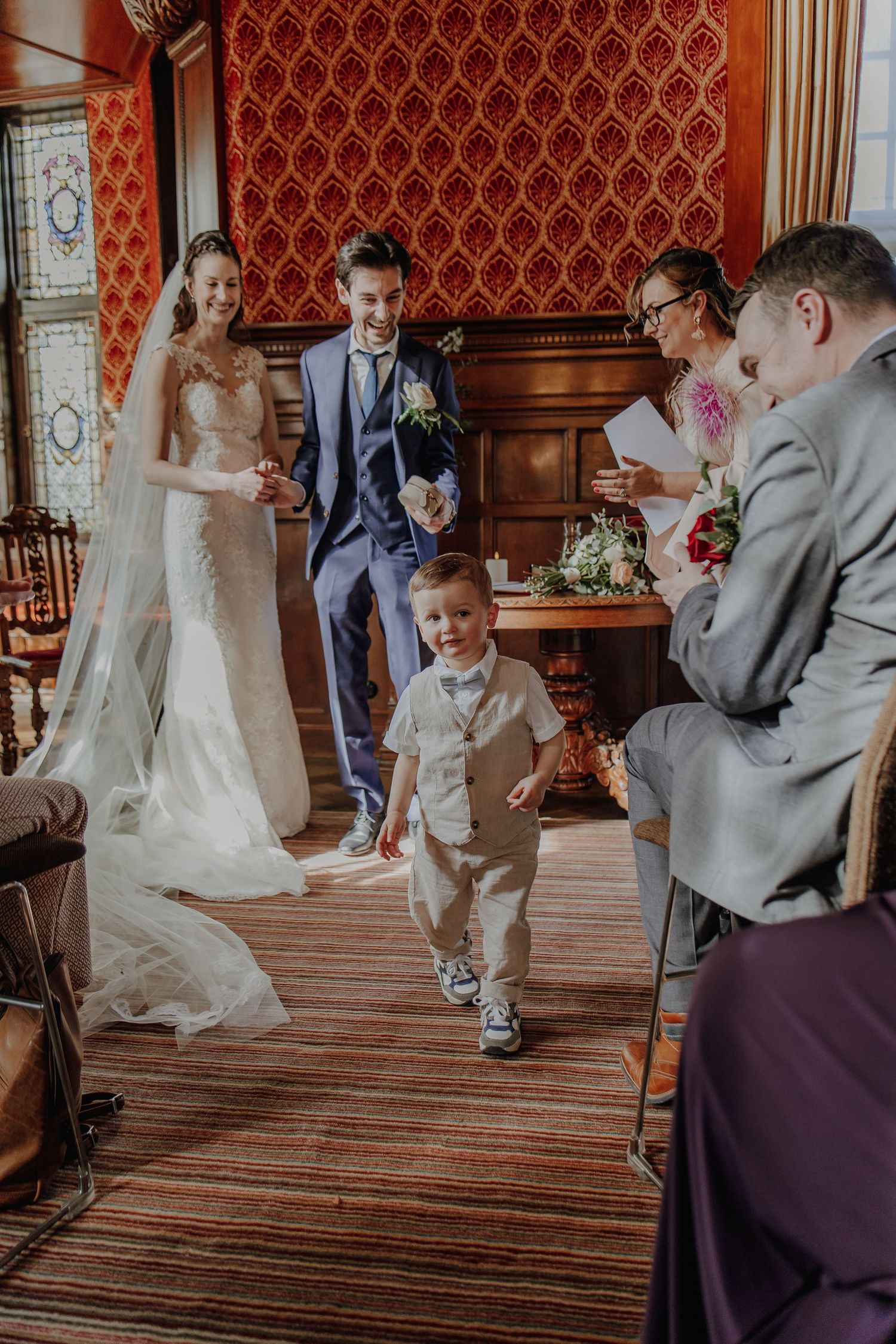 Joyful wedding couple with young ring bearer walking down aisle in elegant venue.