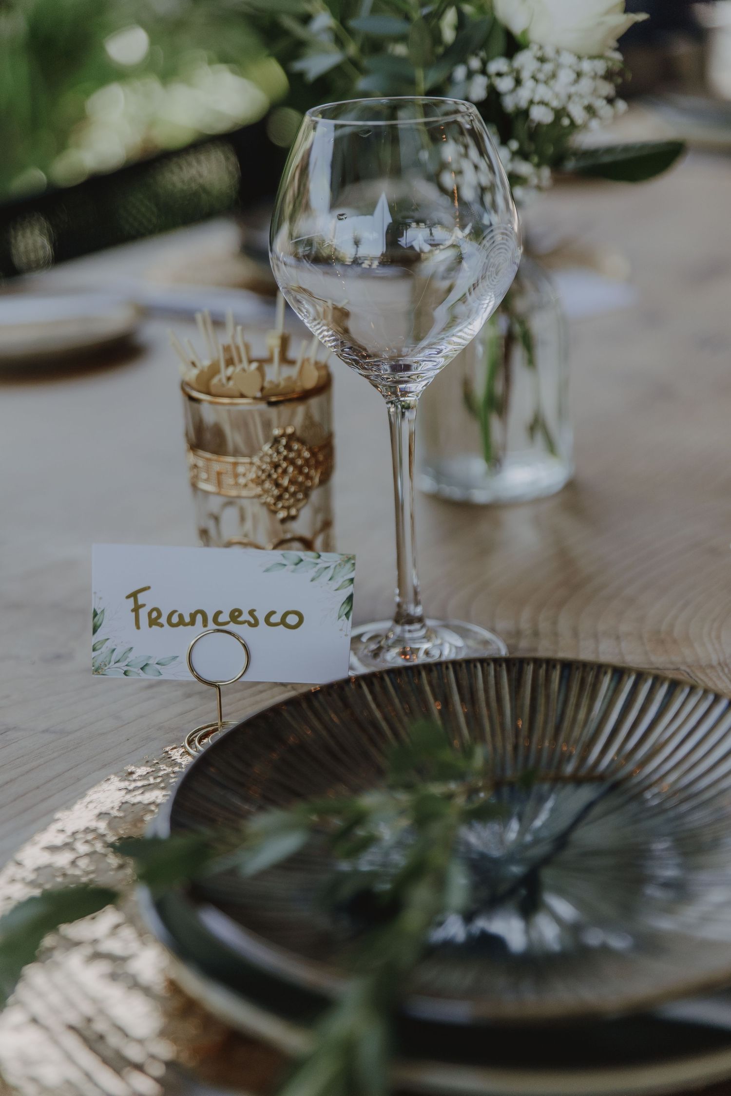 Elegant wedding table setting with wine glass, name card reading Francesco, and greenery decor.