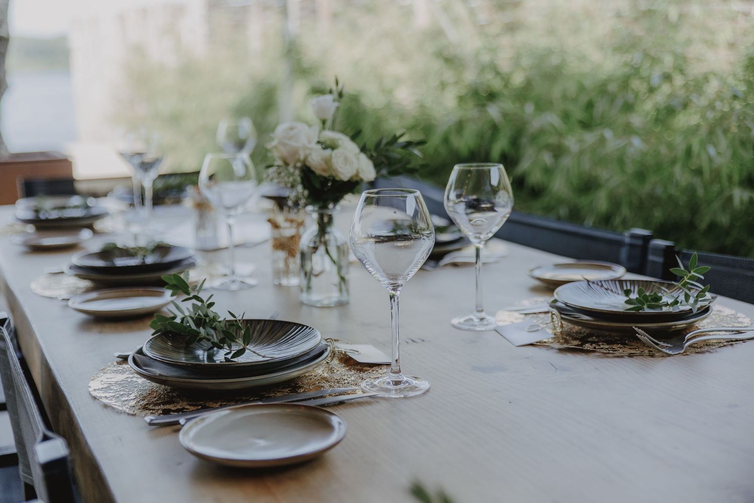 Minimalist wedding reception table set with dark plates, crystal glasses, and white floral centerpieces.