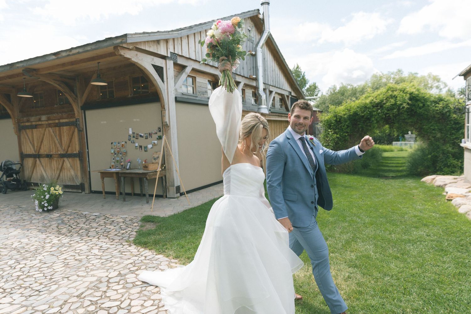 Wedding couple walks on cobblestone path near rustic barn venue.
