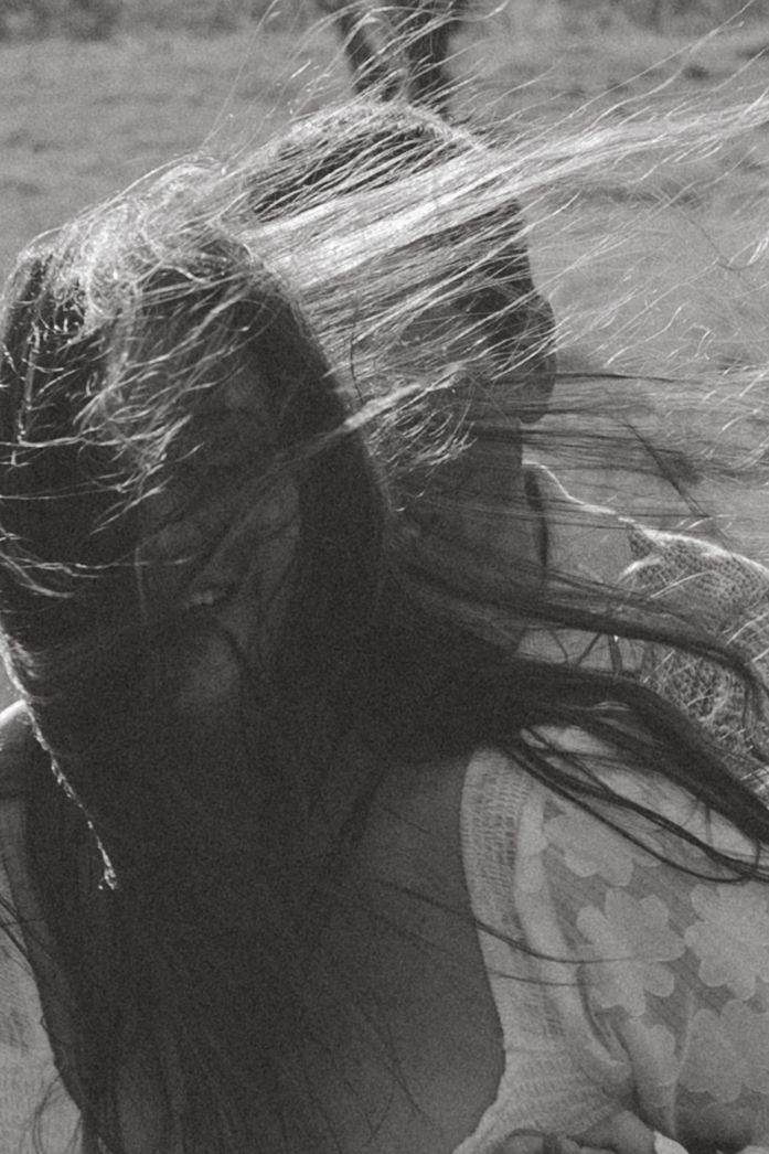 A dramatic black and white photo shows windswept hair flowing against a dark silhouette with a wing tattoo visible.