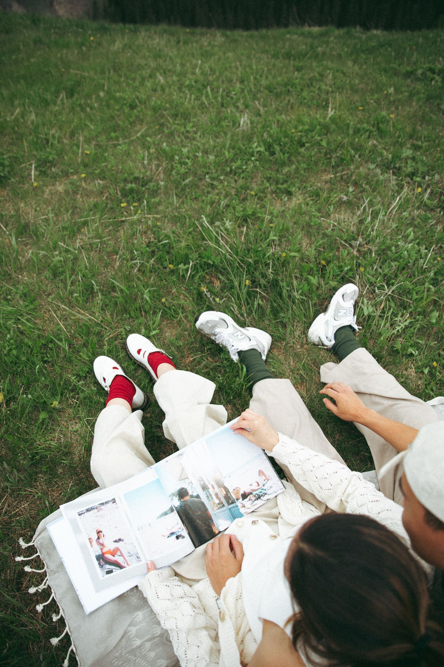 People lying on grass reading a photo album together outdoors.