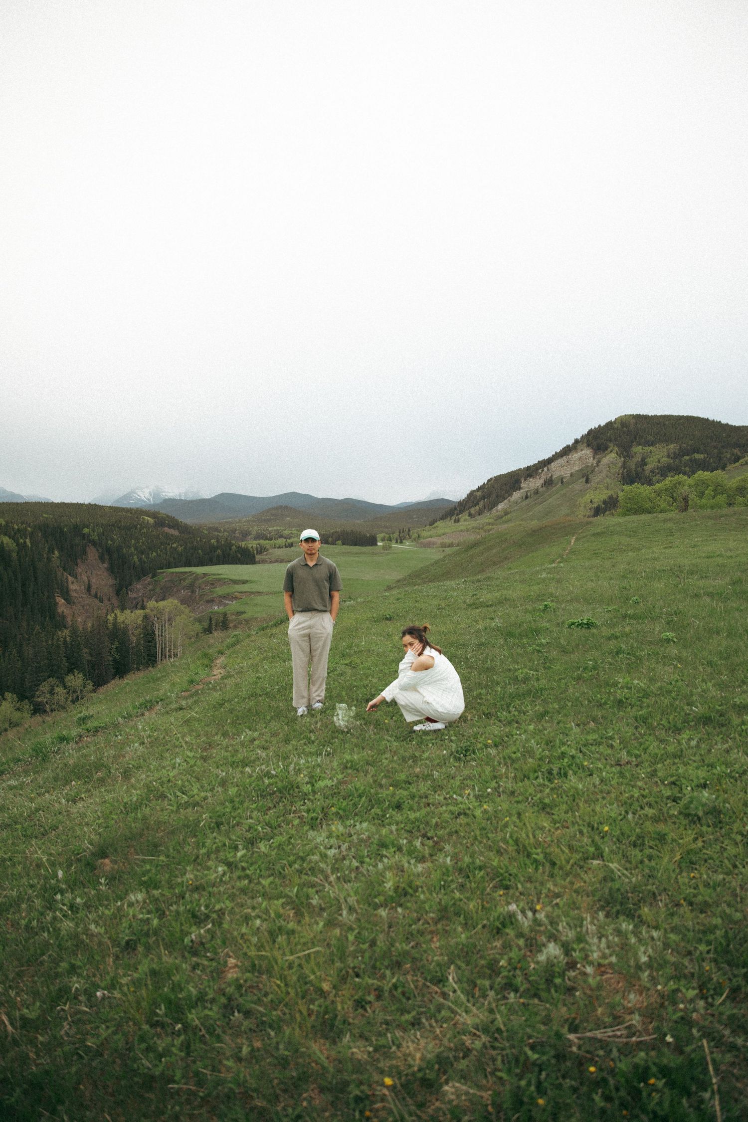 Two people in casual attire standing on a grassy mountain overlook.