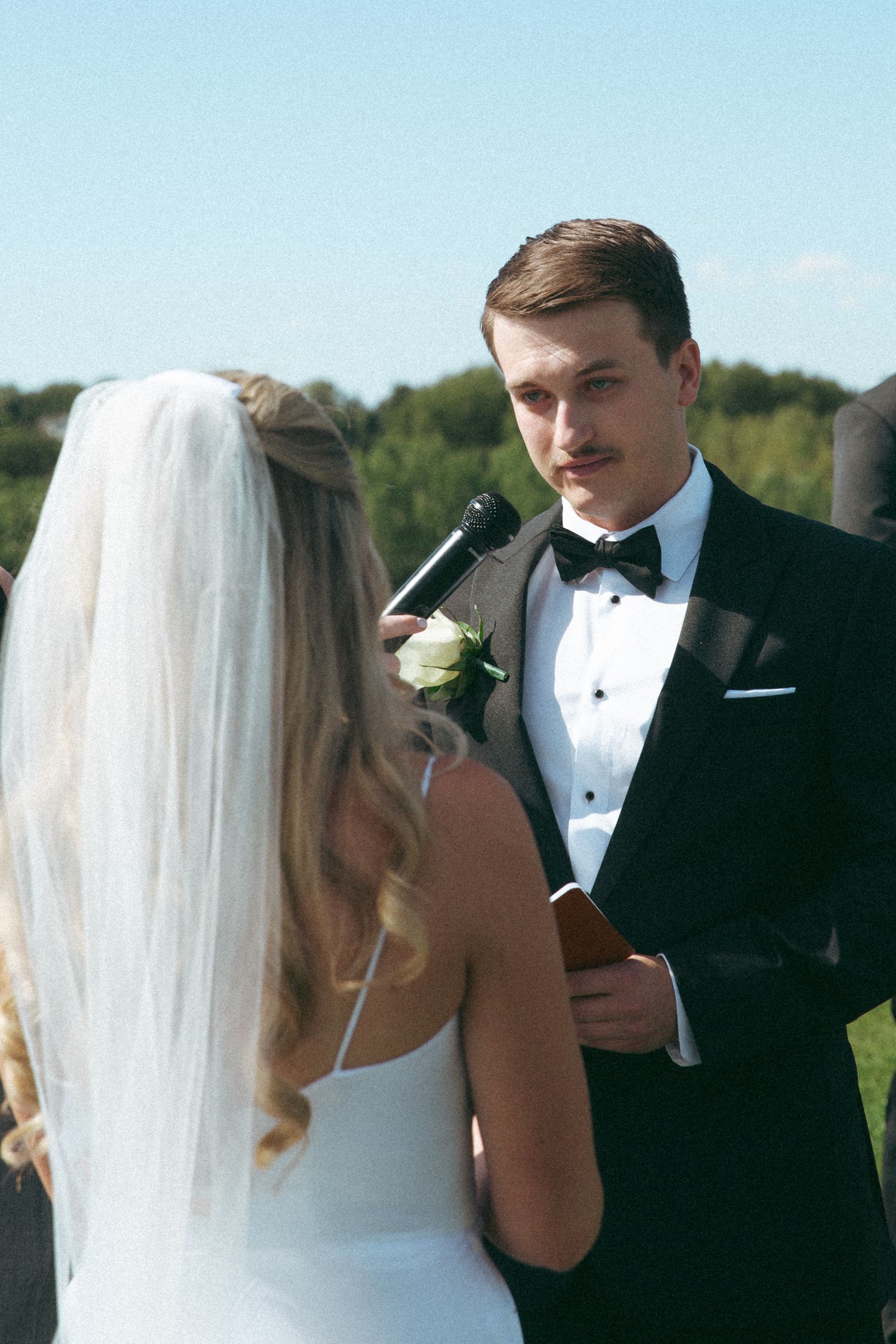 Wedding ceremony exchange of vows at outdoor venue with scenic background.