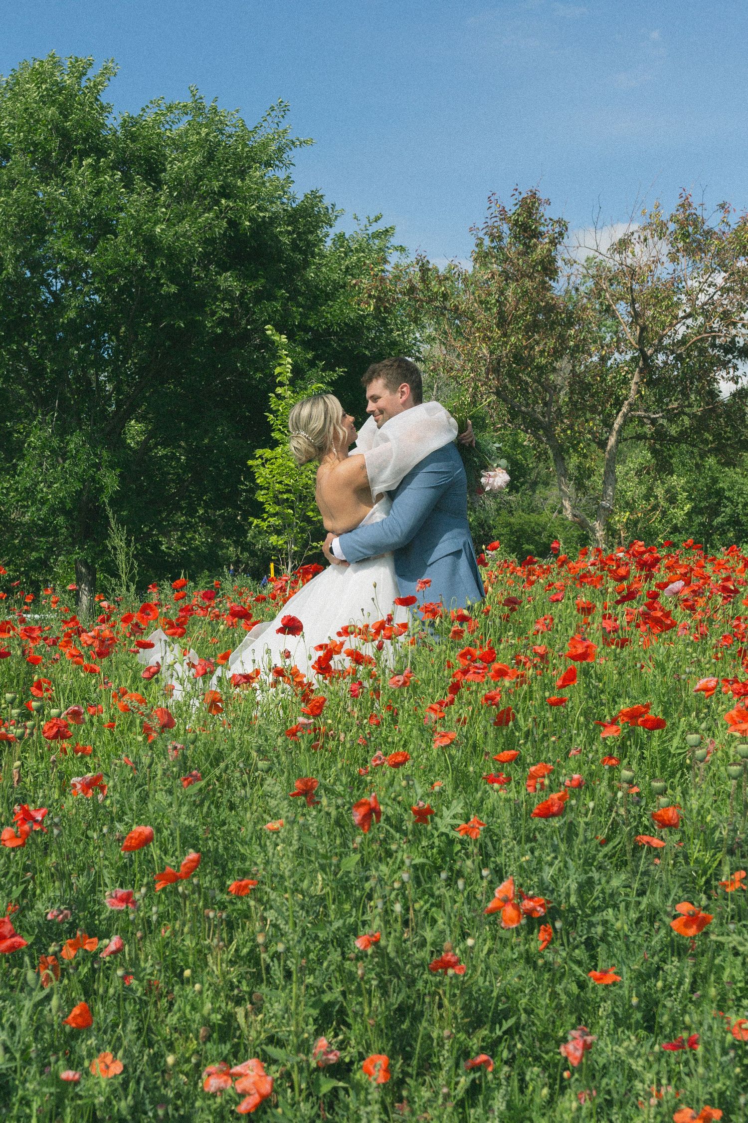 Couple embraces in a vibrant field of red poppies on their wedding day.