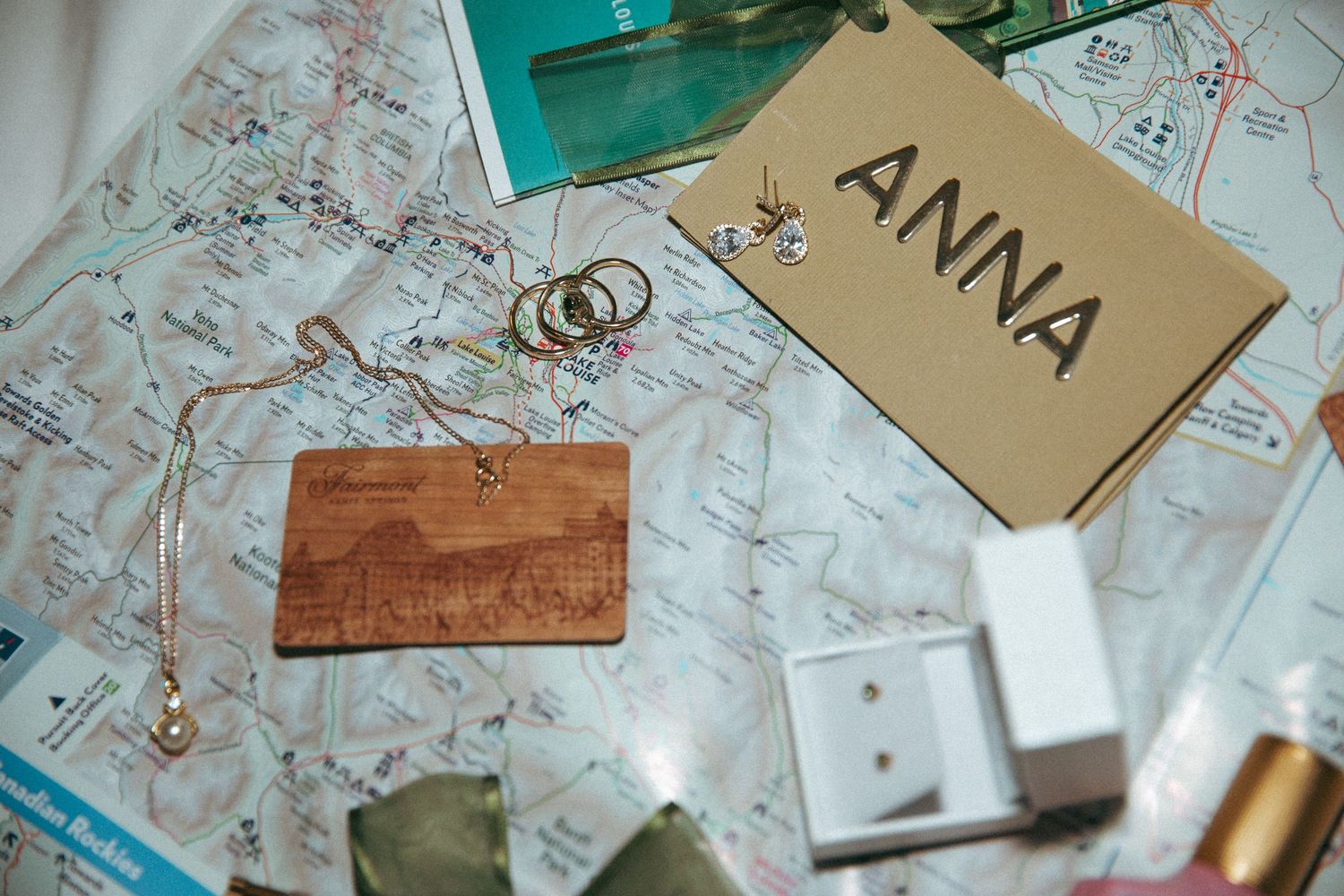A tag labeled 'ANNA' rests on a map alongside a wooden card, gold rings and various travel accessories.