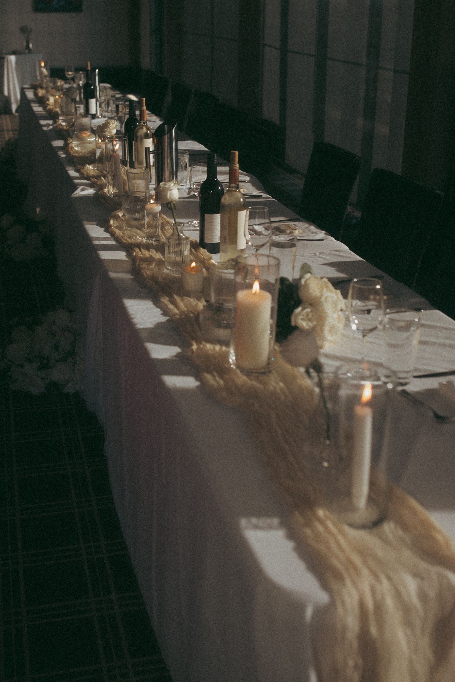 Elegant wedding reception table decorated with candles and fabric runners in dim lighting.