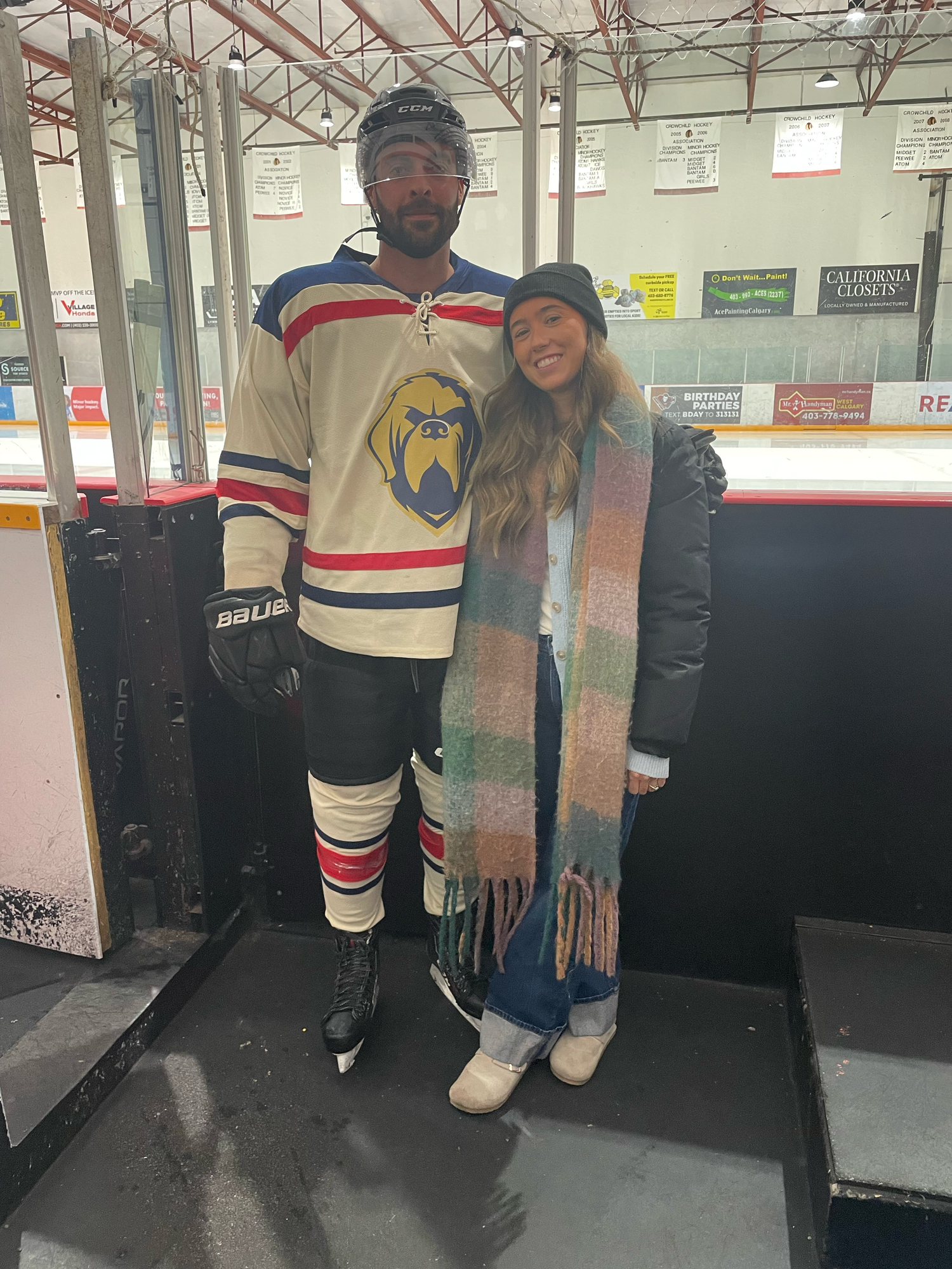Hockey player in vintage-style jersey posing with companion at an indoor ice rink.