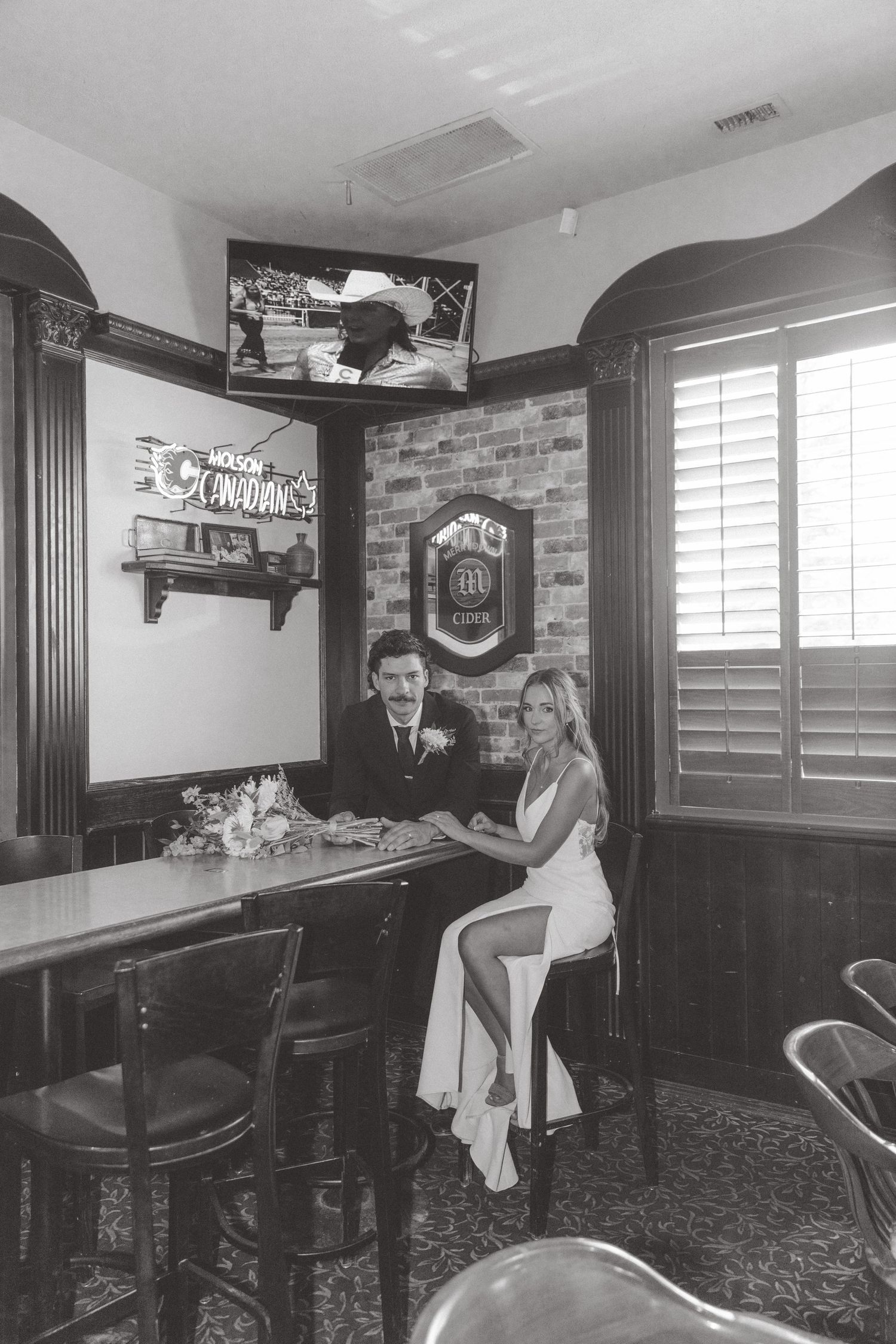 Black and white photo of bride and groom sitting together at a bar in a classic pub setting.