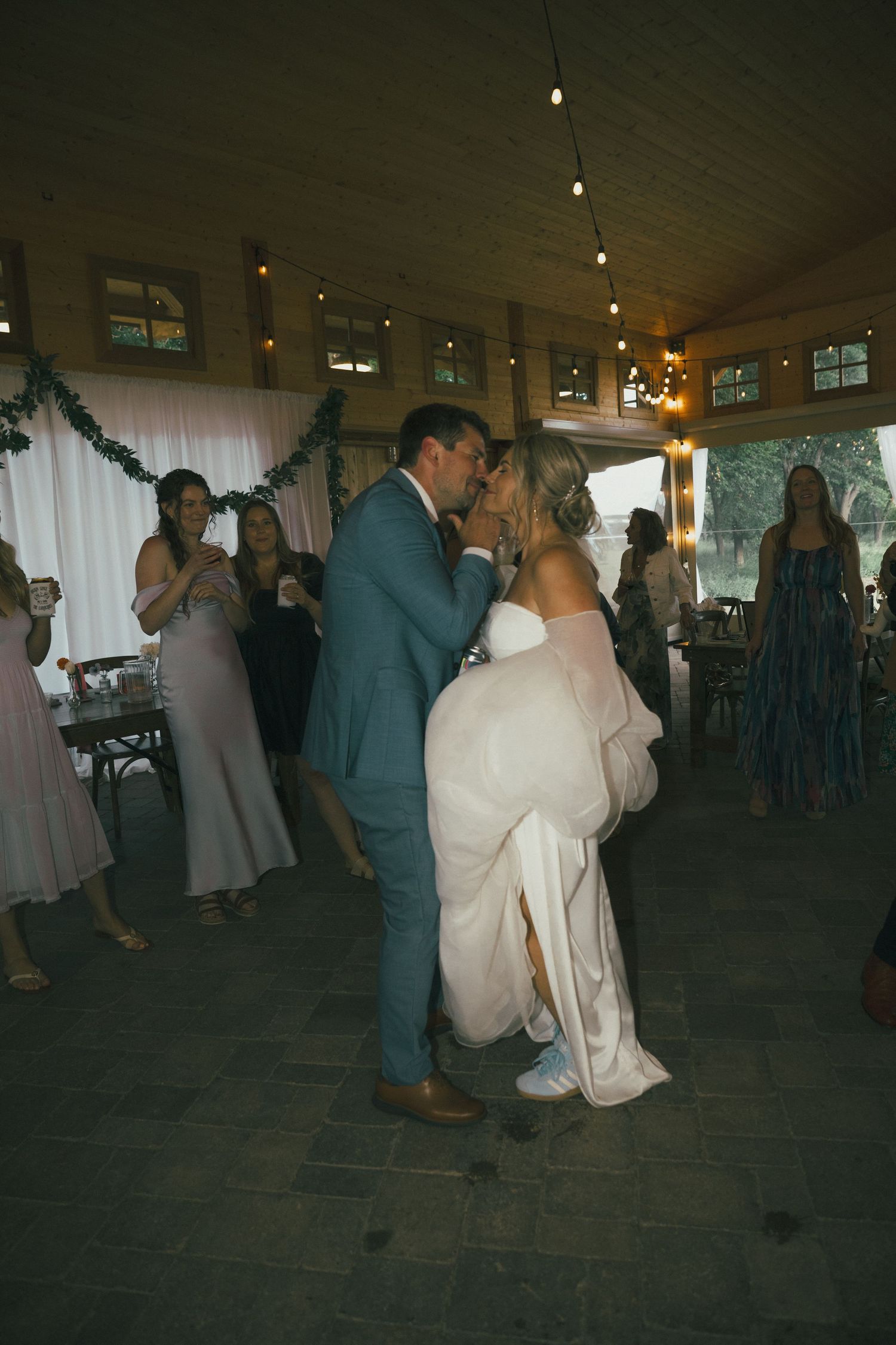 Wedding reception dance floor under a white tent with string lights and dancing guests.