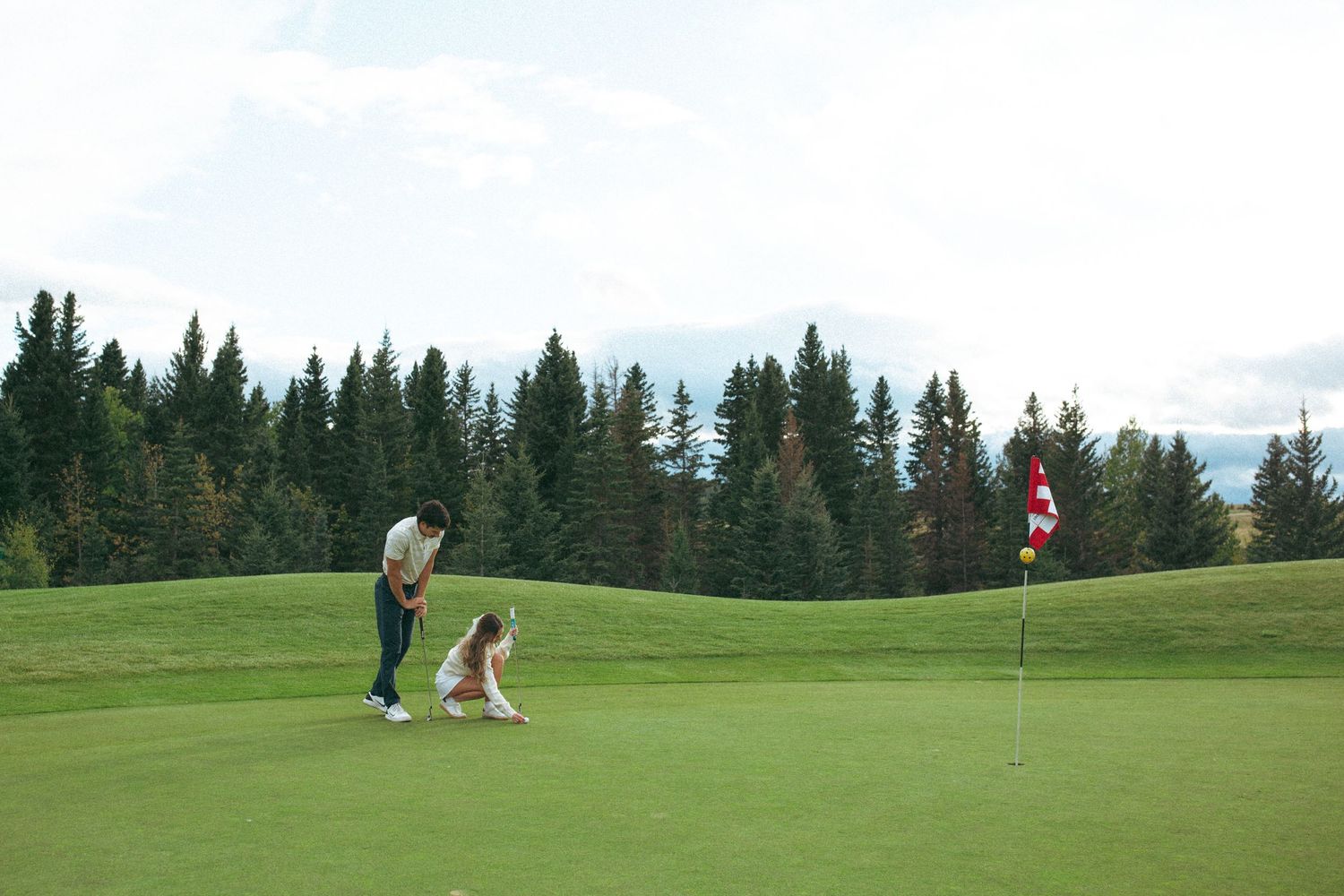 Two people practicing their golf game on a putting green with mountain scenery.