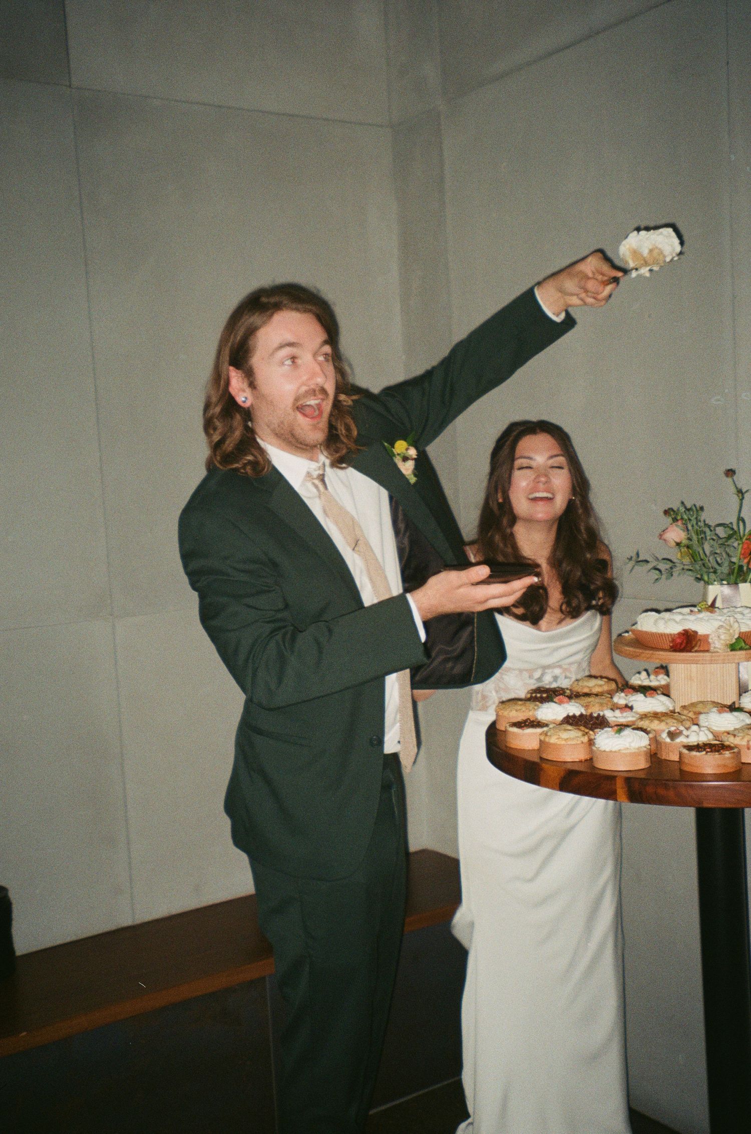 Wedding couple shares a playful moment at their reception while posing near a table of desserts.