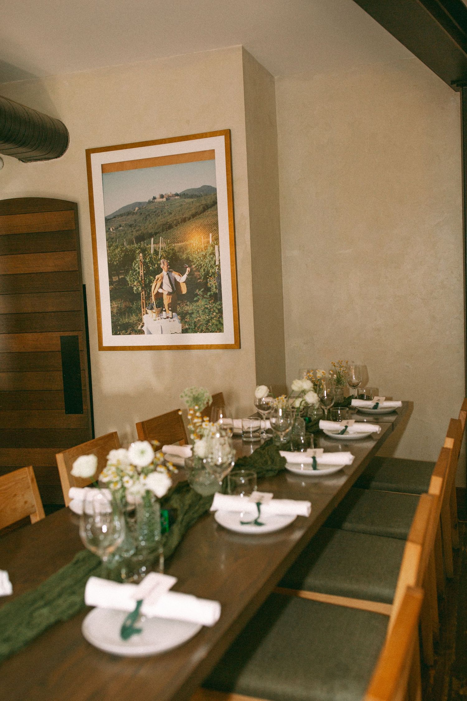 An elegant table setting with white plates, green runners, and floral centerpieces in a dining room with framed artwork.