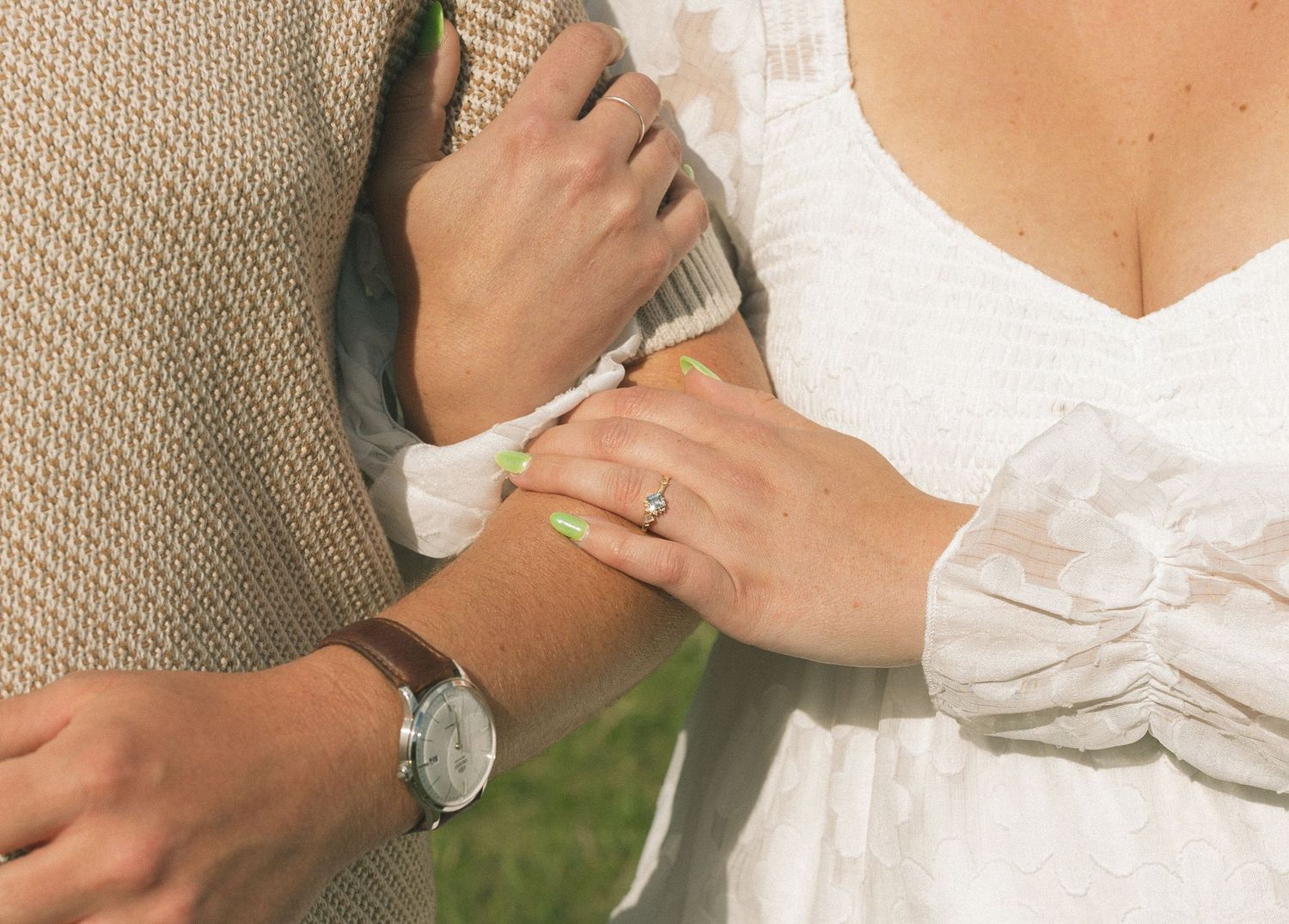 Close-up of hands wearing a watch and ring against a light-colored fabric background.