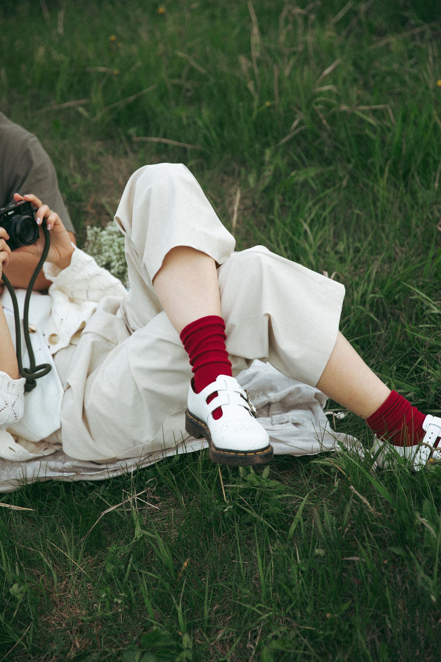 Person in white dress and red socks lying on grass with camera.