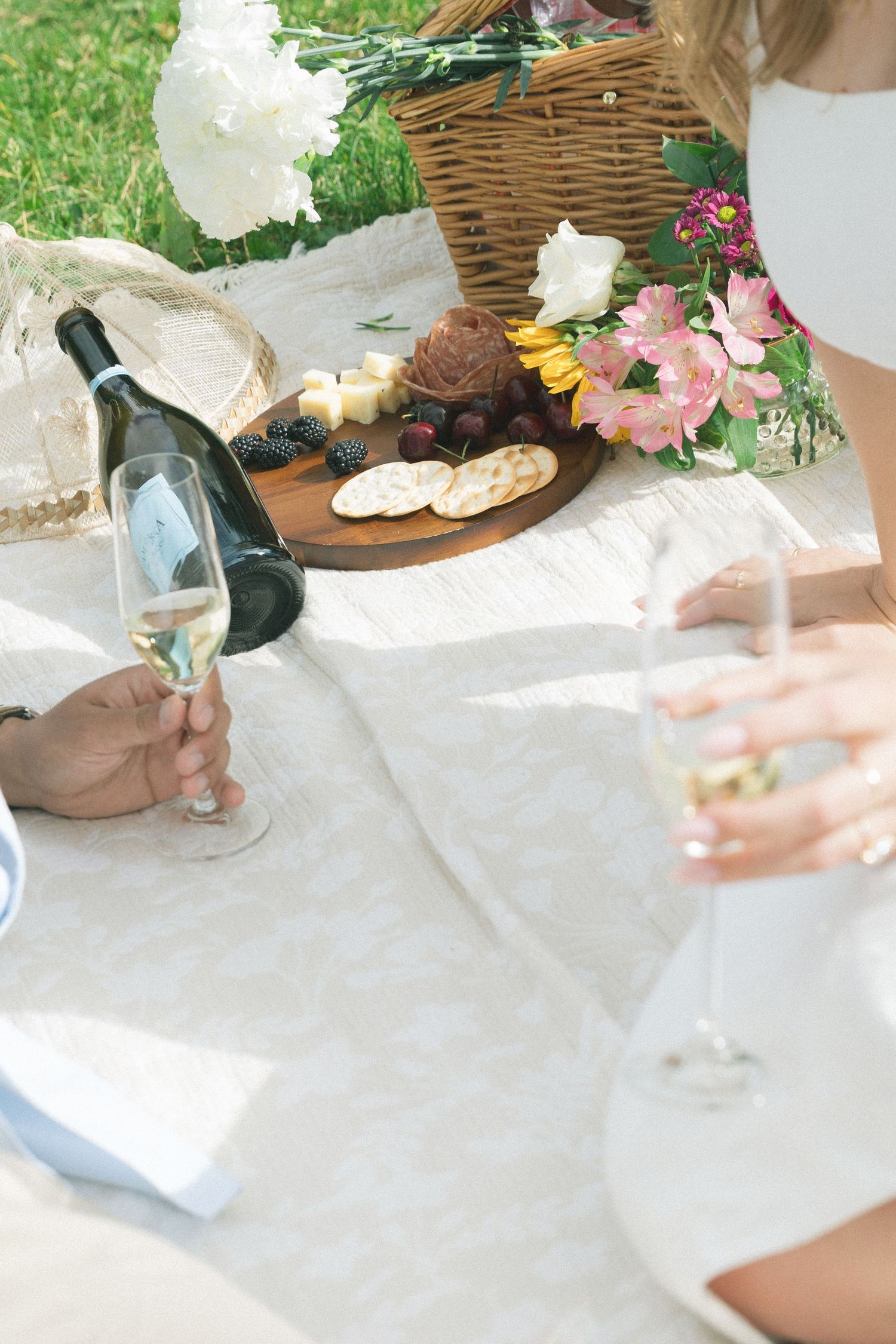 A picnic setting with a white blanket and wicker basket on green grass.