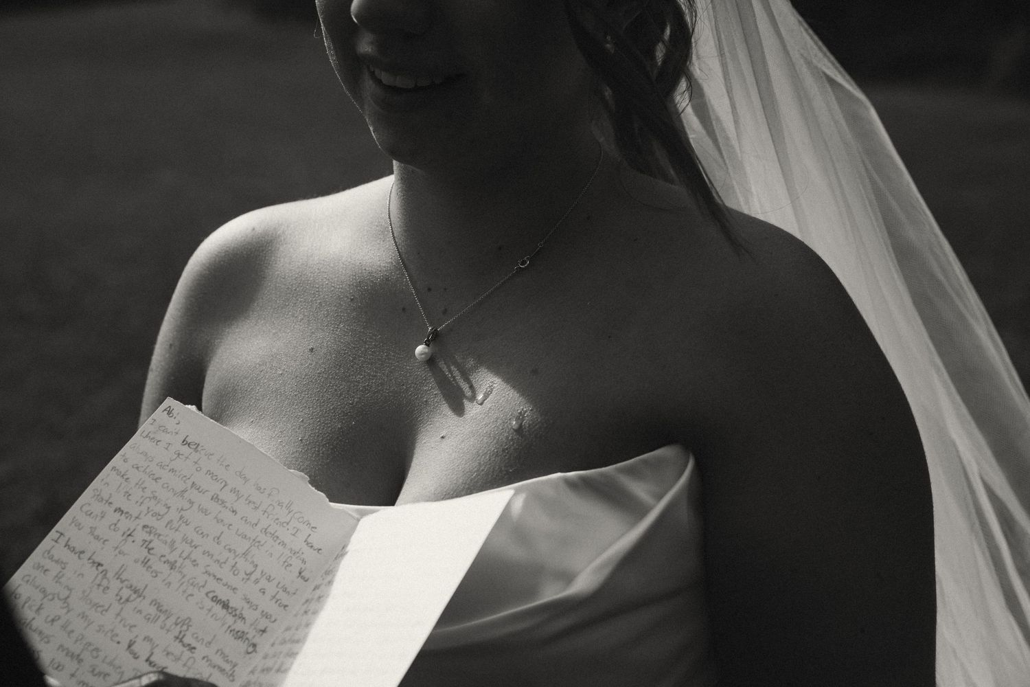 Black and white close-up of a bride in a strapless gown reading a handwritten letter on her wedding day.