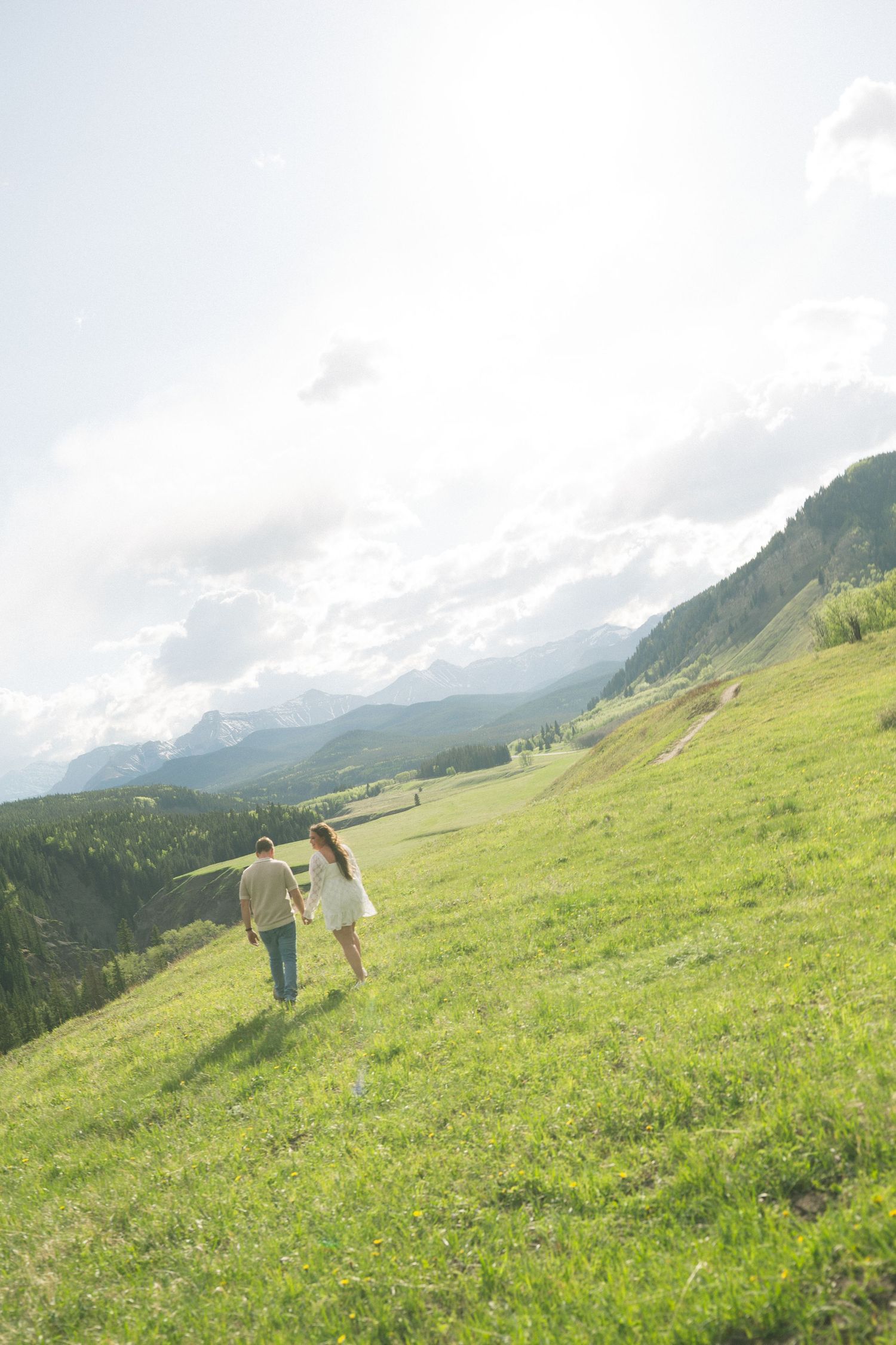 Two people walking hand in hand on a scenic mountain hillside with stunning valley views and cloudy skies.