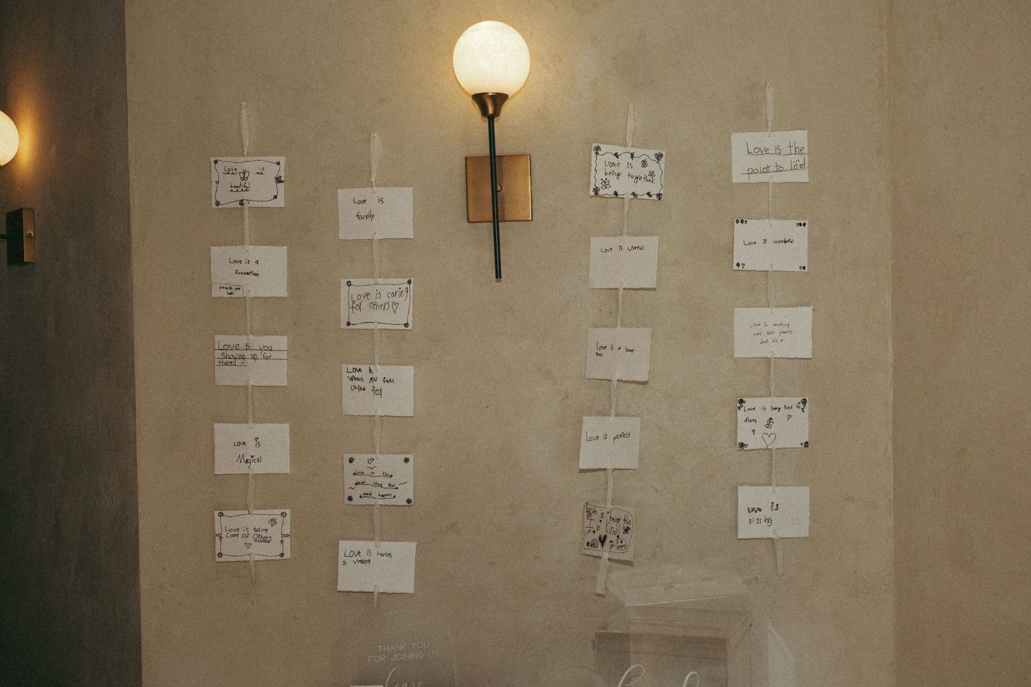 White paper notes arranged in a grid pattern on a beige wall with a single wall sconce light fixture.
