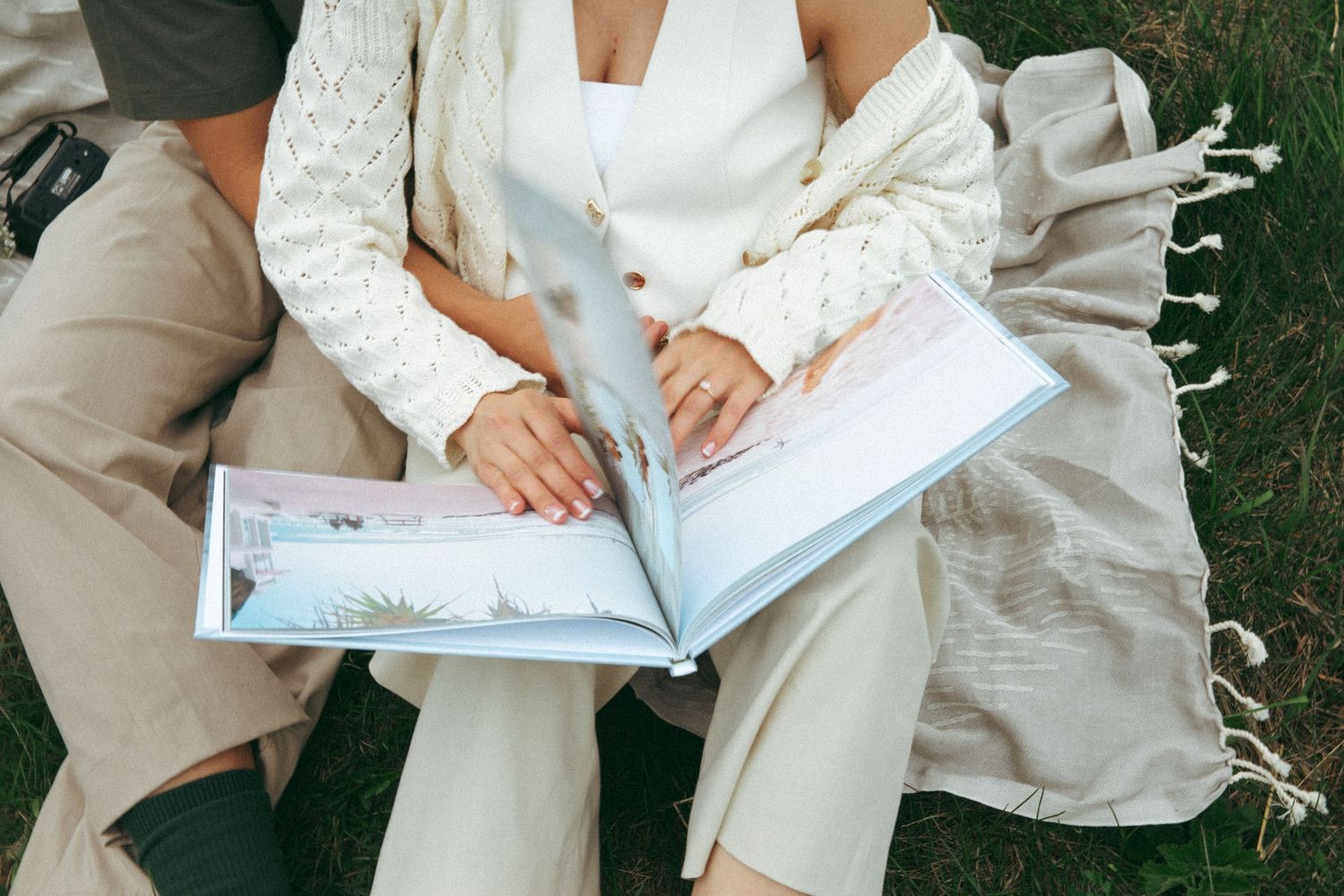 Couple looking through a photo album while sitting on grass outdoors.