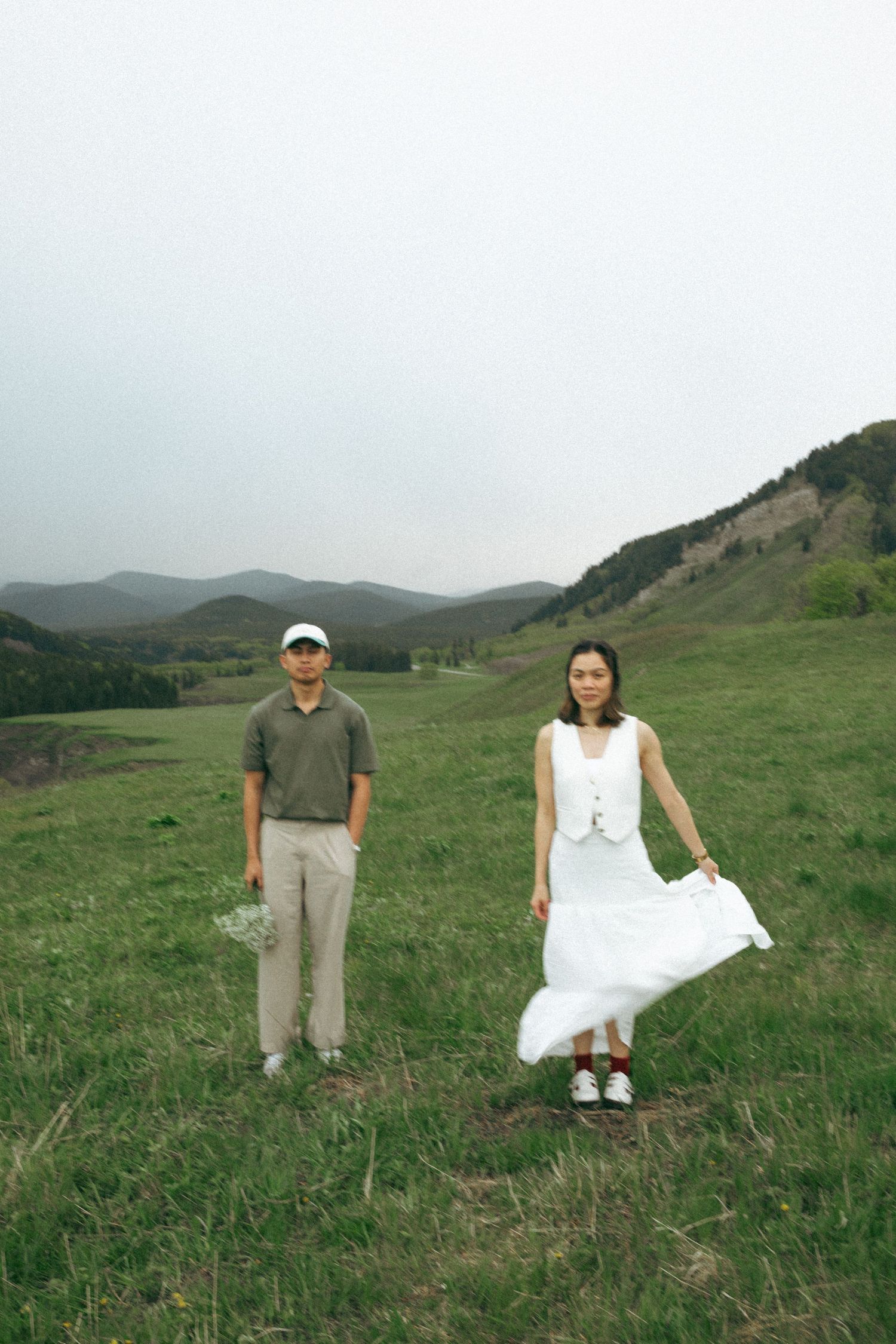 Couple in contrasting outfits standing together on a green mountainside.