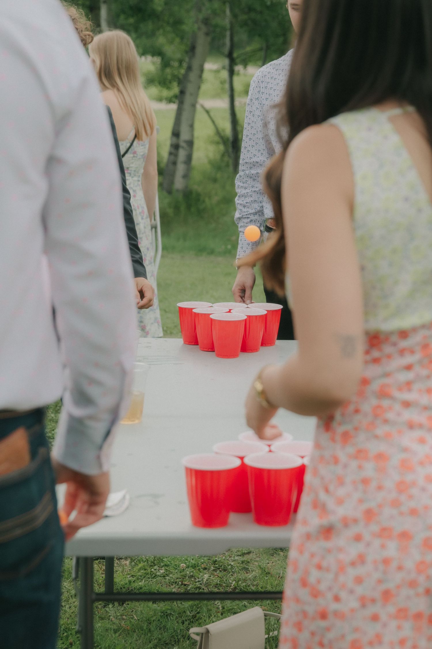 Wedding guests playing beer pong with red Solo cups on a white table at an outdoor reception.