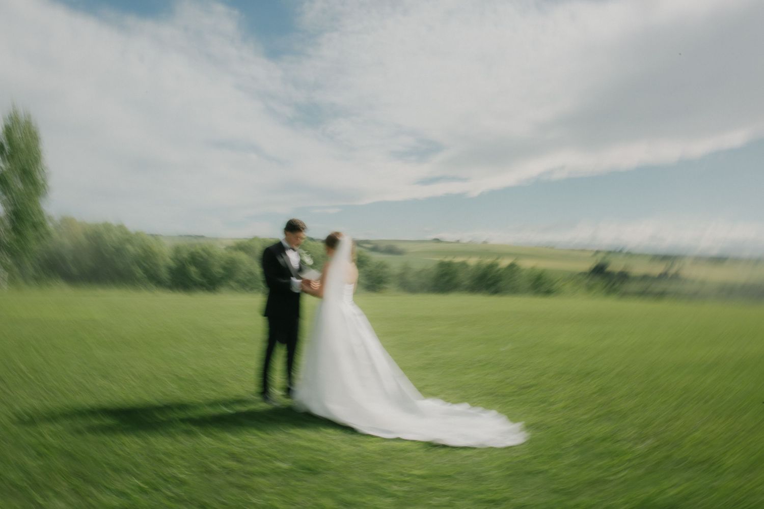 Bride and groom standing together on lush green lawn with scenic countryside backdrop on their wedding day.