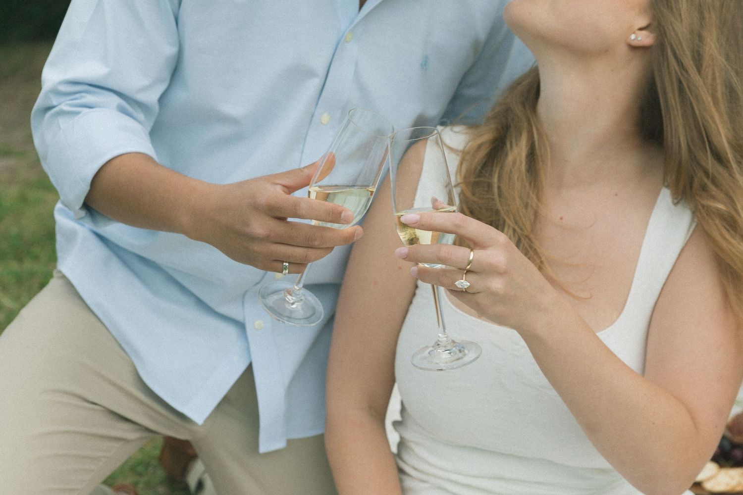 Two people sitting outdoors holding wine glasses and dressed in casual summer attire with white and blue clothing.