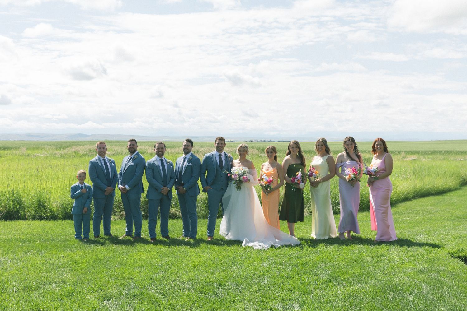 Wedding party lined up in an open green field on a sunny day.