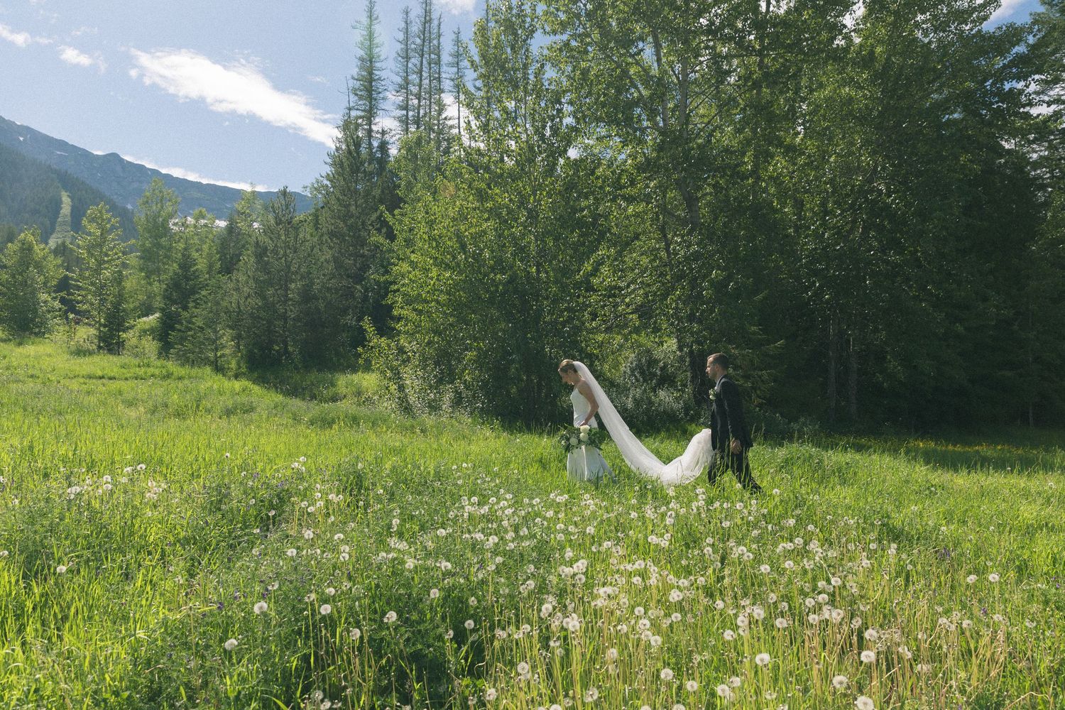 Couple in wedding attire walking through a mountain meadow filled with wildflowers.