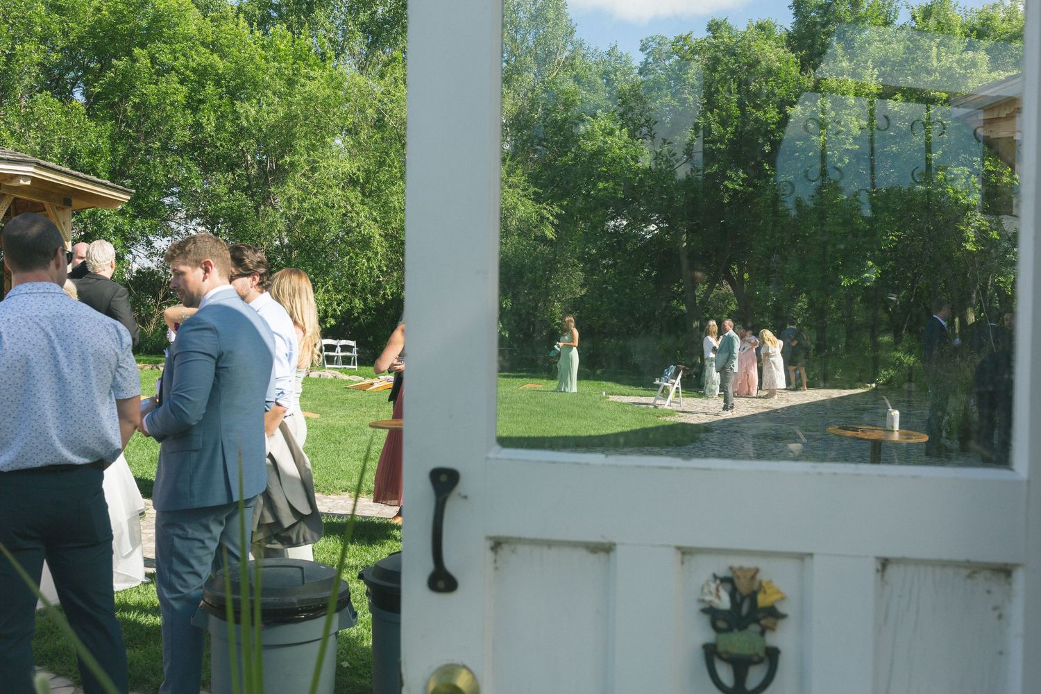 Wedding ceremony takes place under white pillars in an outdoor garden setting.